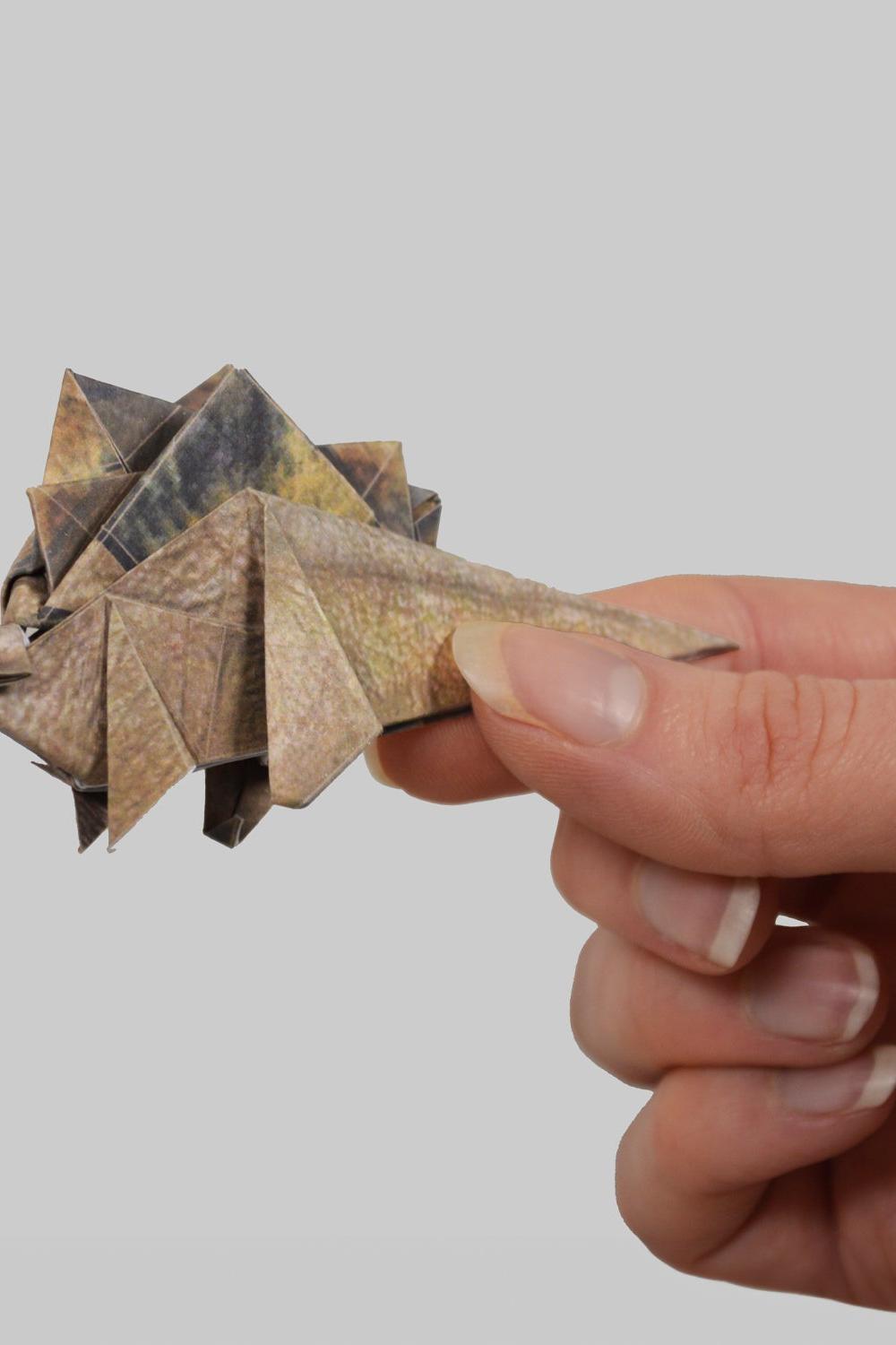 Hand holding a small origami dinosaur against a plain background