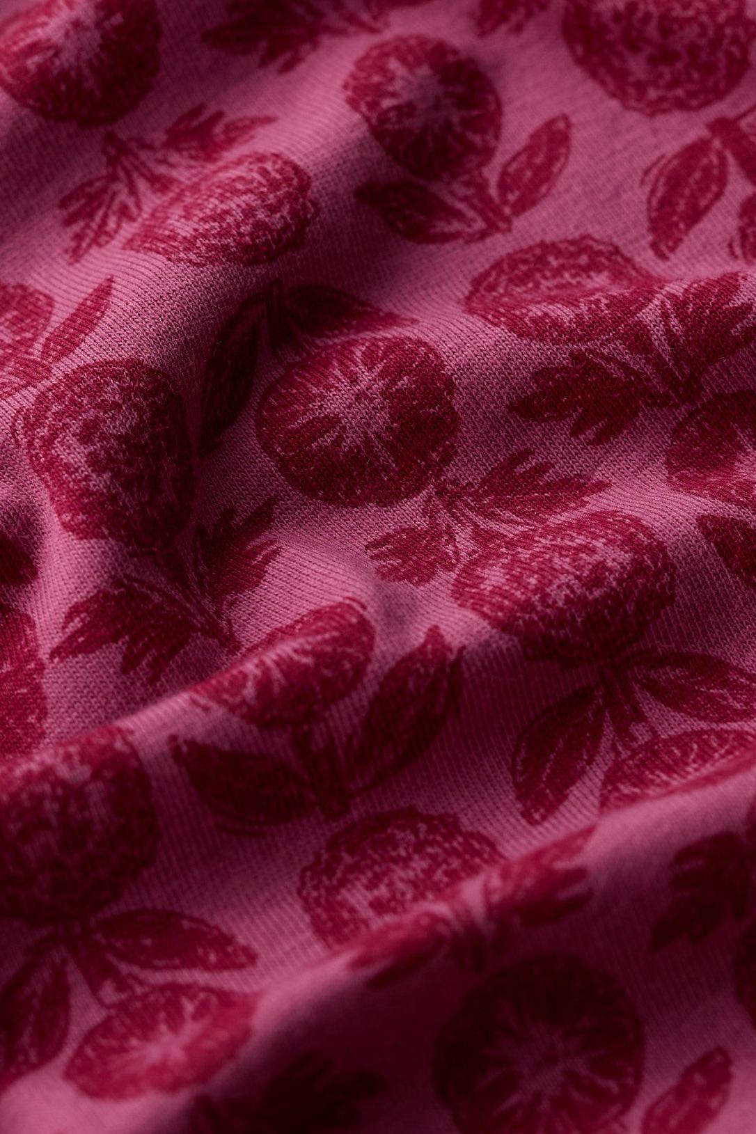 A close-up of draped fabric with a dark red floral and fruit pattern on a magenta-pink background.