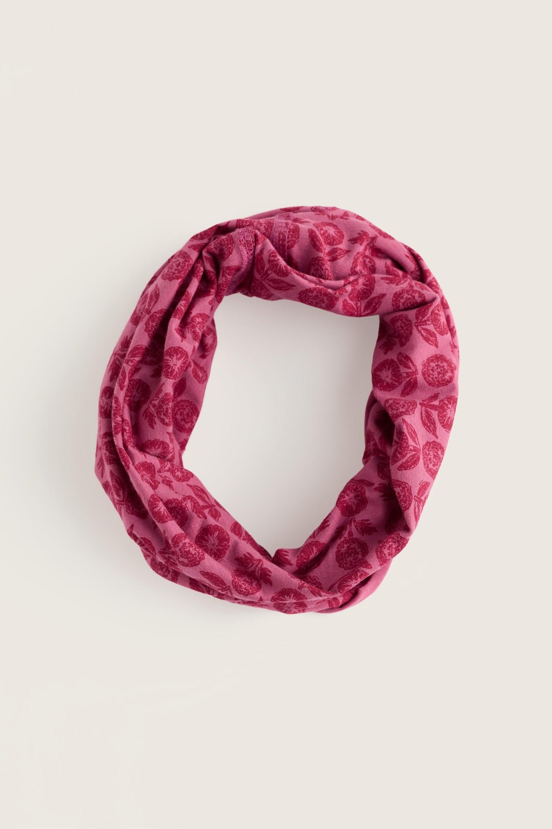 A dusty rose pink infinity scarf with a tonal floral pattern, photographed flat on a light beige background.