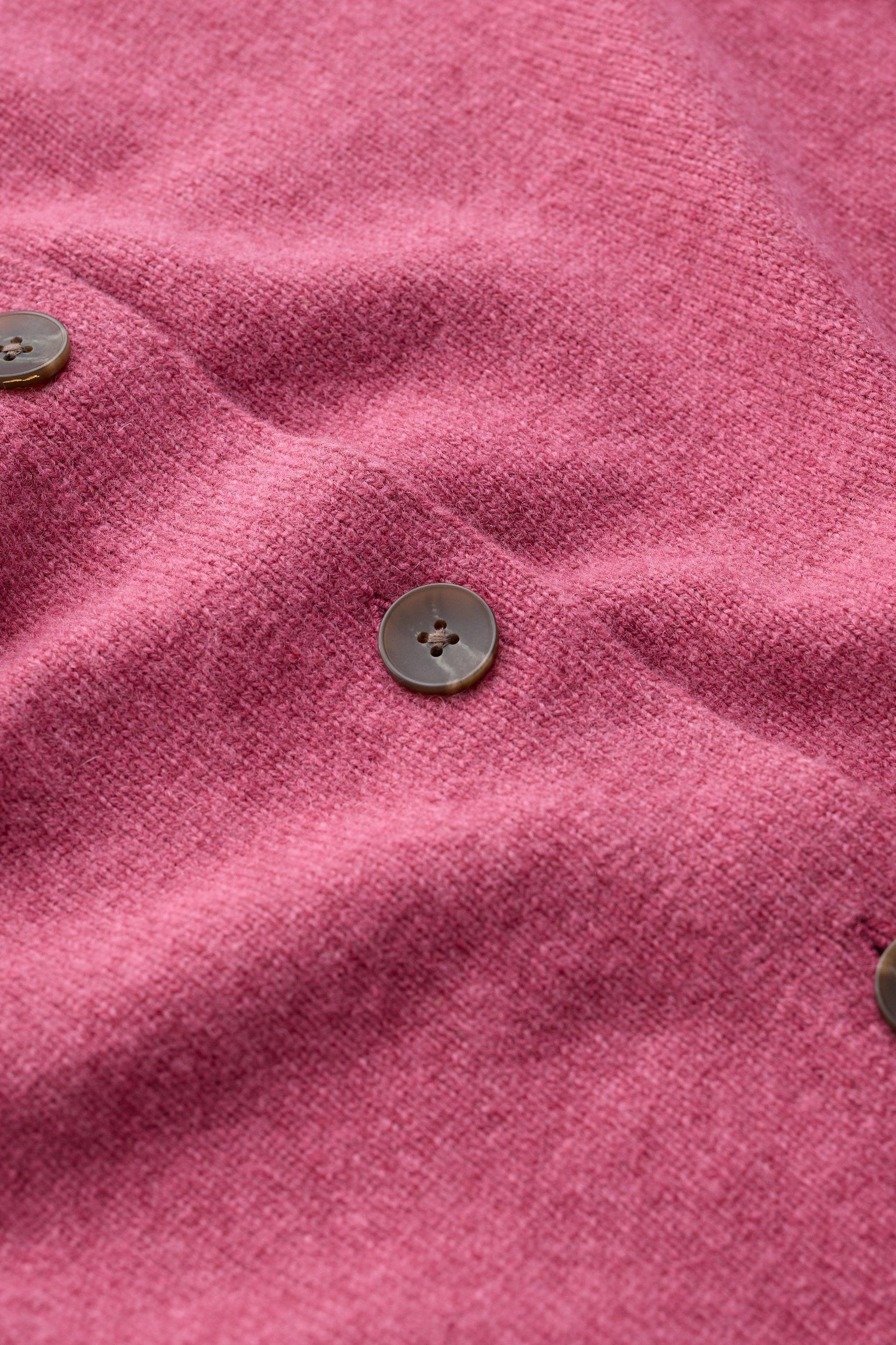 Close-up of a pink knit fabric with three visible dark brown buttons, showing the soft texture and drape of the material.