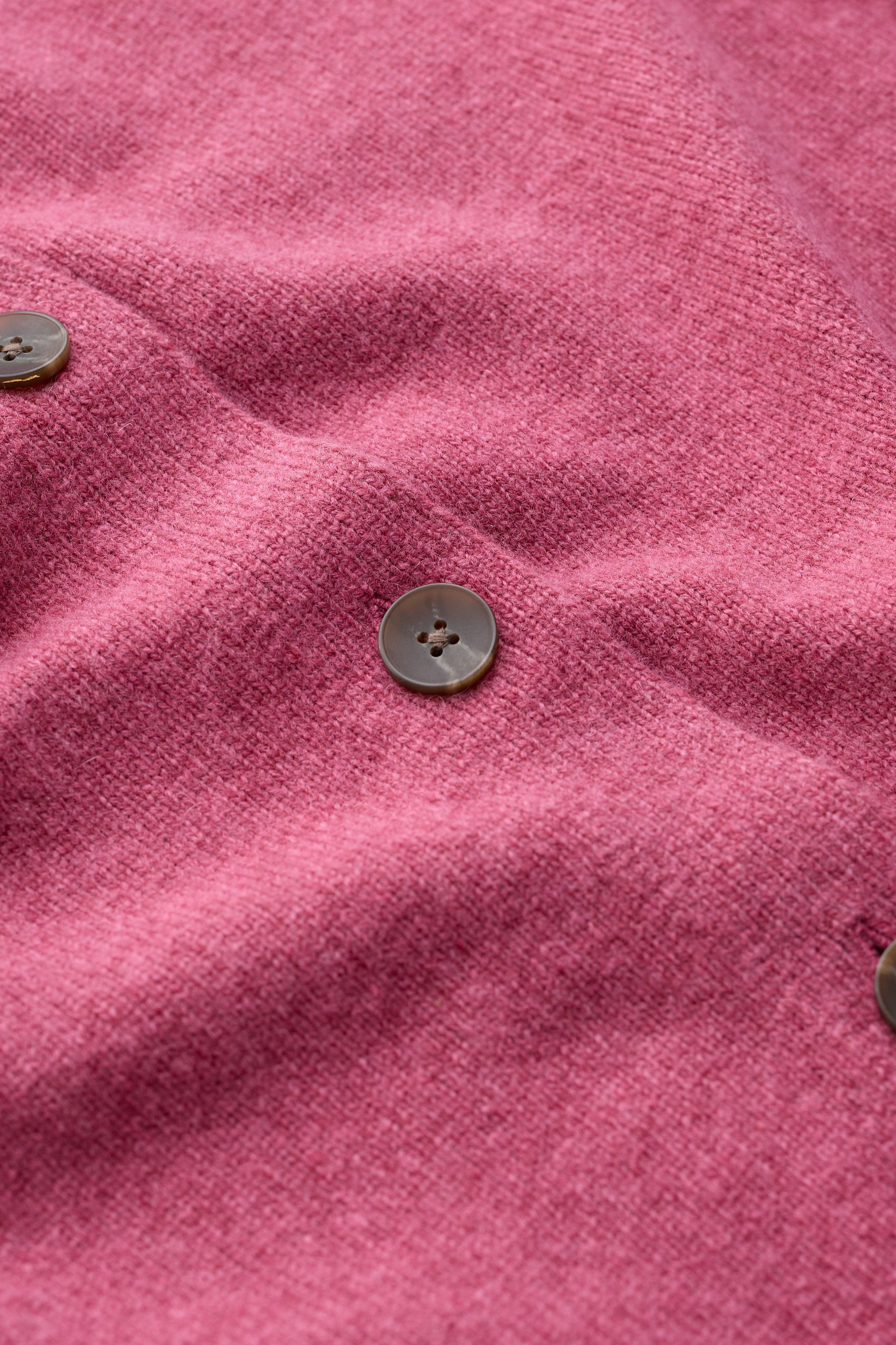 Close-up of a pink knit fabric with three visible dark brown buttons, showing the soft texture and drape of the material.