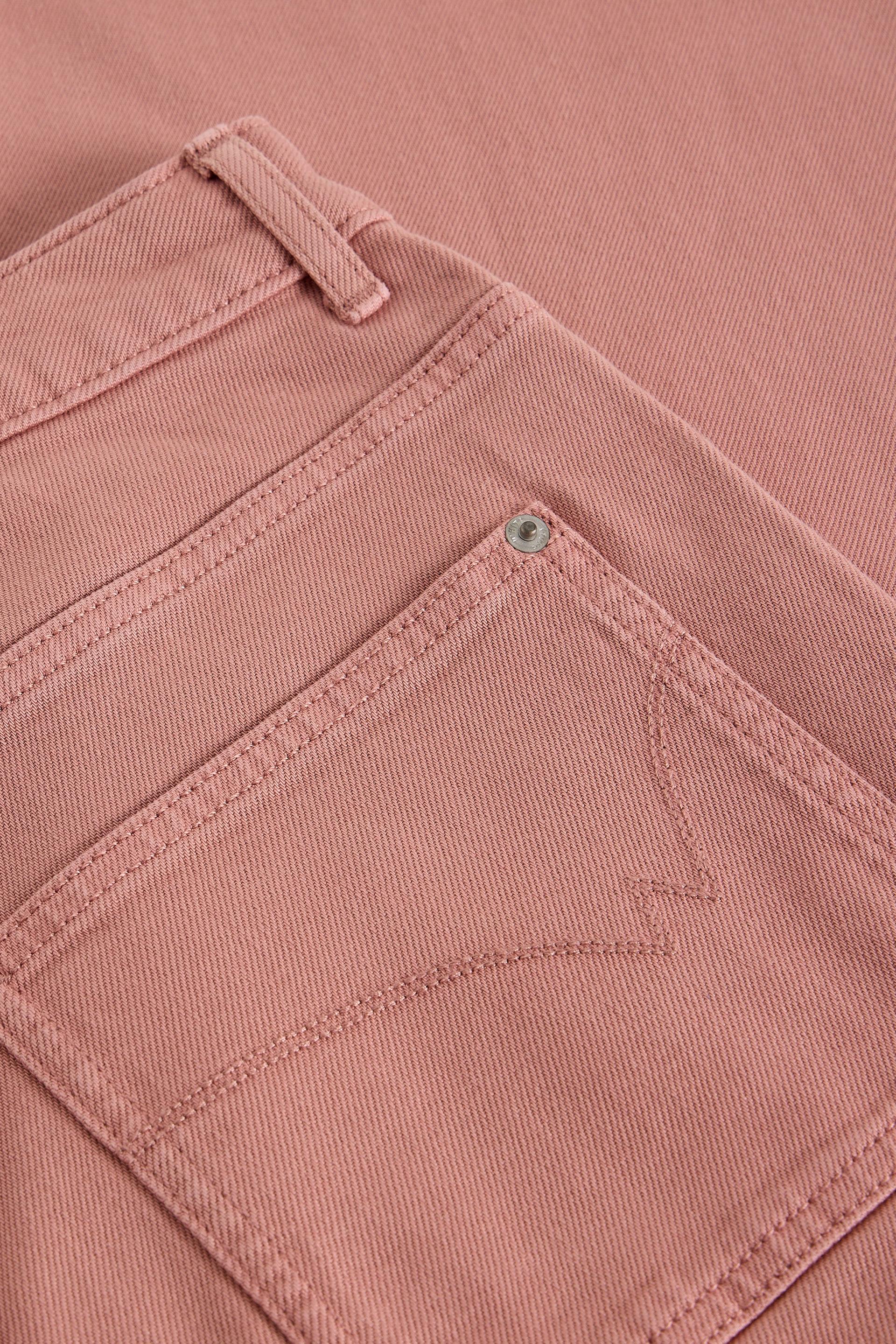 Close-up of a dusty pink organic cotton denim pocket with metal rivet detail.