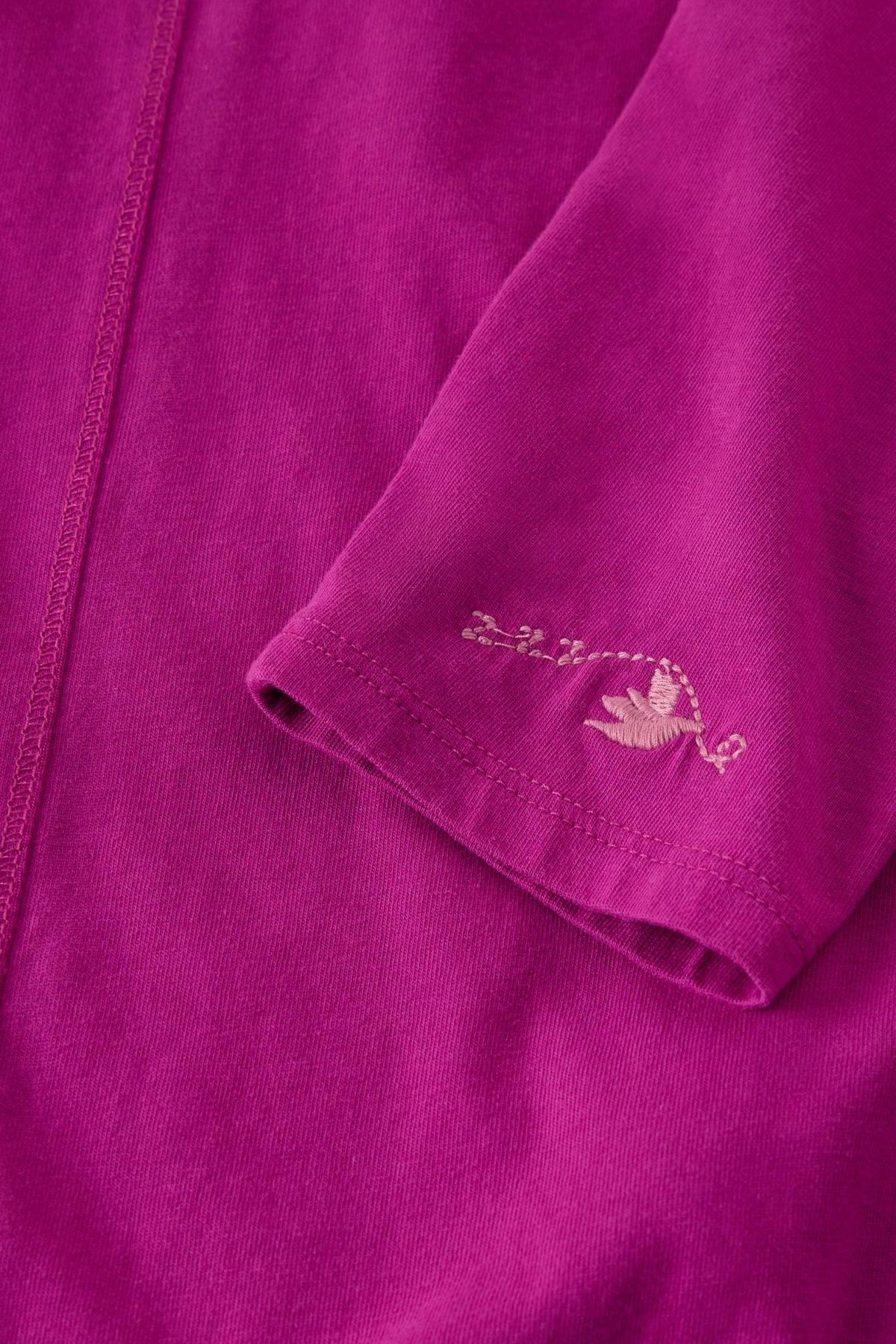 Close-up of a pink organic cotton White Stuff pyjama top with embroidered bird detail on the sleeve.