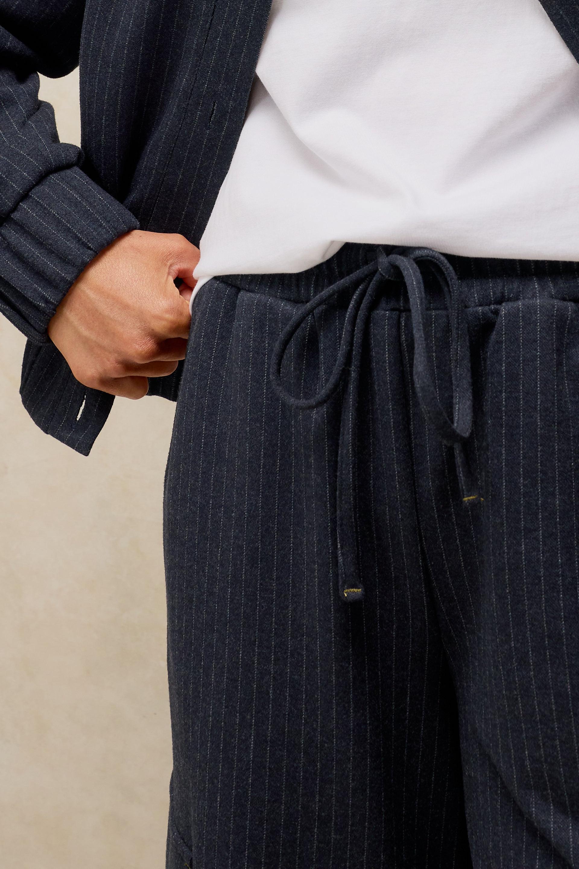 Close-up of a person wearing dark navy pinstriped trousers with a drawstring waist, styled with a white shirt and a matching dark cardigan.