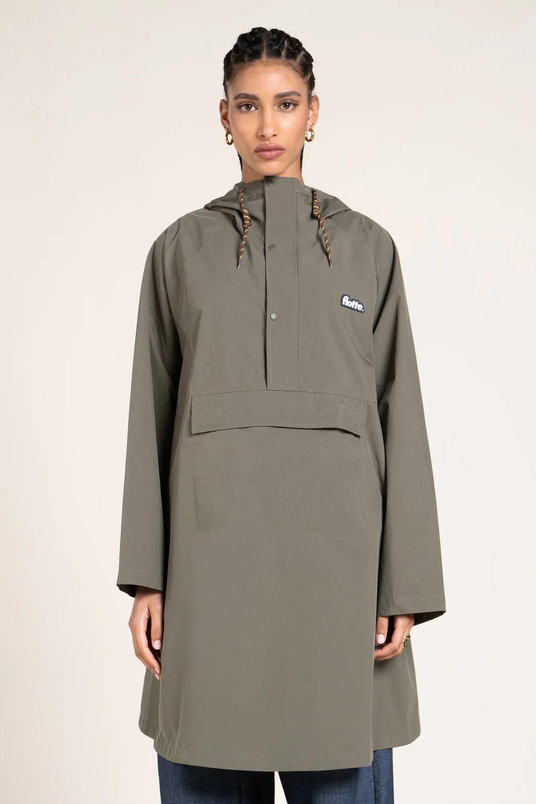 Person wearing a green Flotte raincoat with logo on a beige background