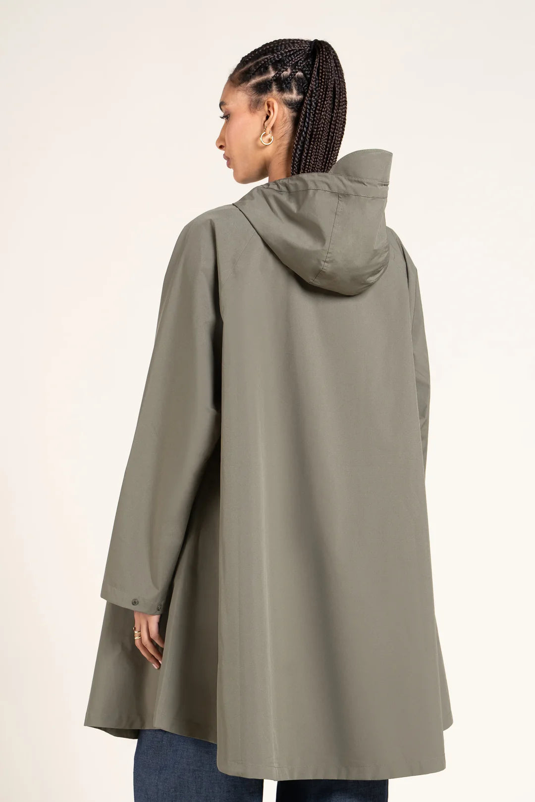 Person wearing a long, Khaki raincoat with a hood on a plain background