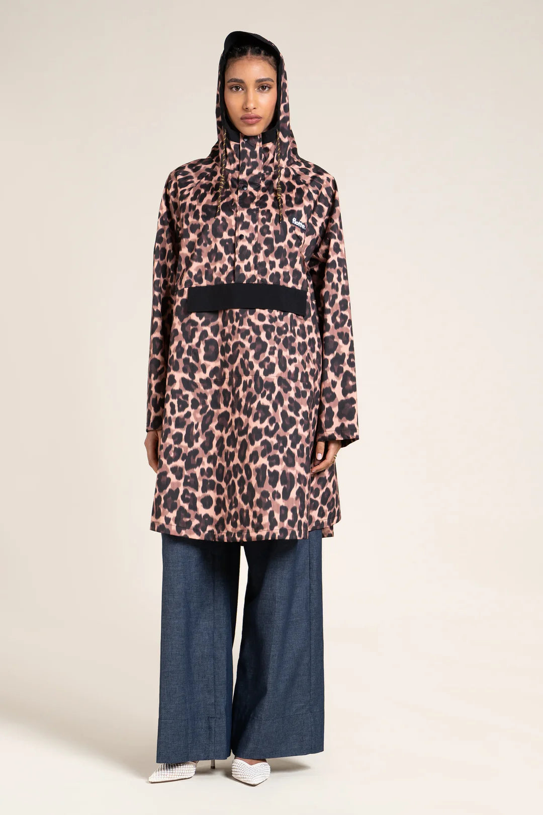 Person wearing a leopard print raincoat and blue pants on a beige background