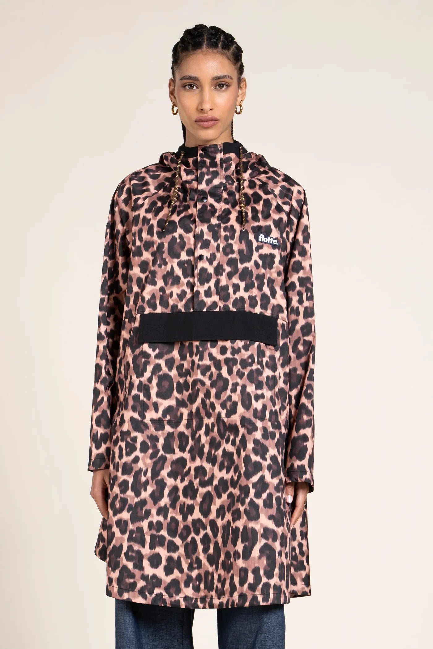 Person wearing a leopard print raincoat with a black pocket pouch on a beige background