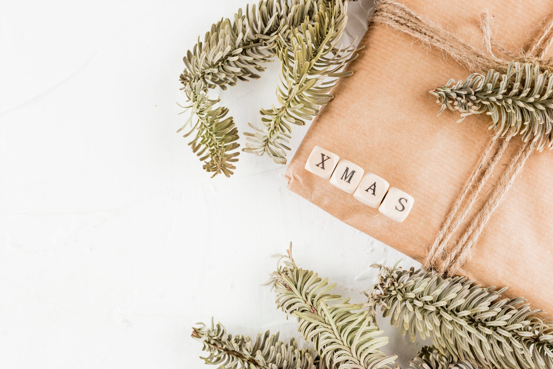 Gift wrapped in brown paper with string, surrounded by pine branches on a white background.