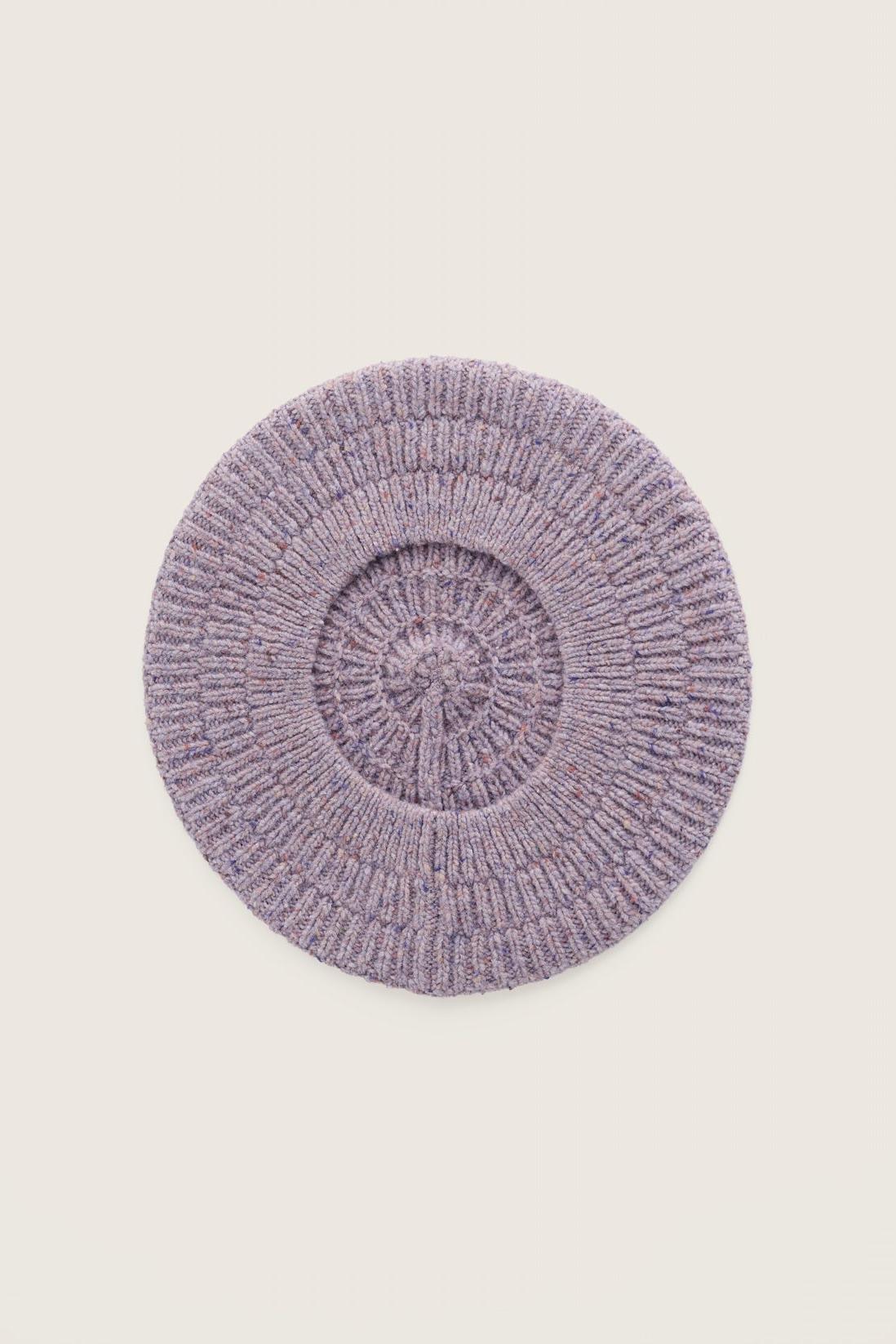 A top-down view of a textured purple merino wool beret hat against a light neutral background.