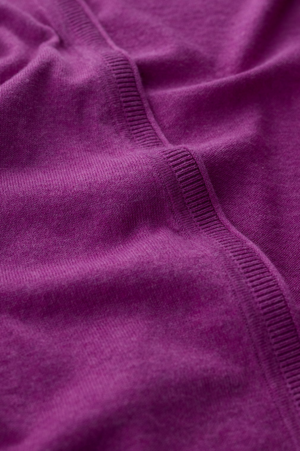 Close-up of a deep purple organic cotton knit fabric with a ribbed seam detail.