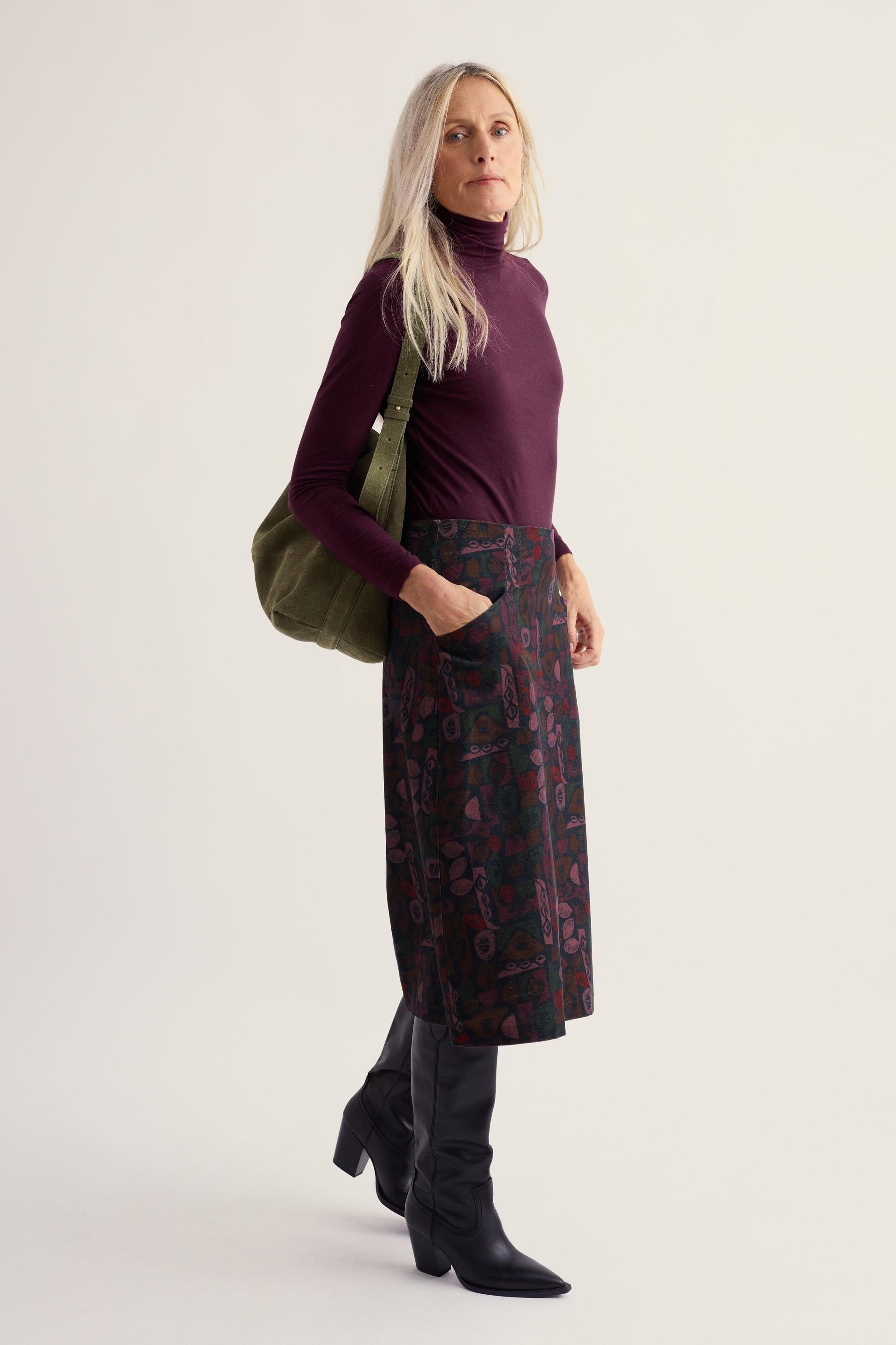 Woman wearing a purple organic cotton roll neck top by Seasalt Cornwall with a patterned skirt and olive green shoulder bag.