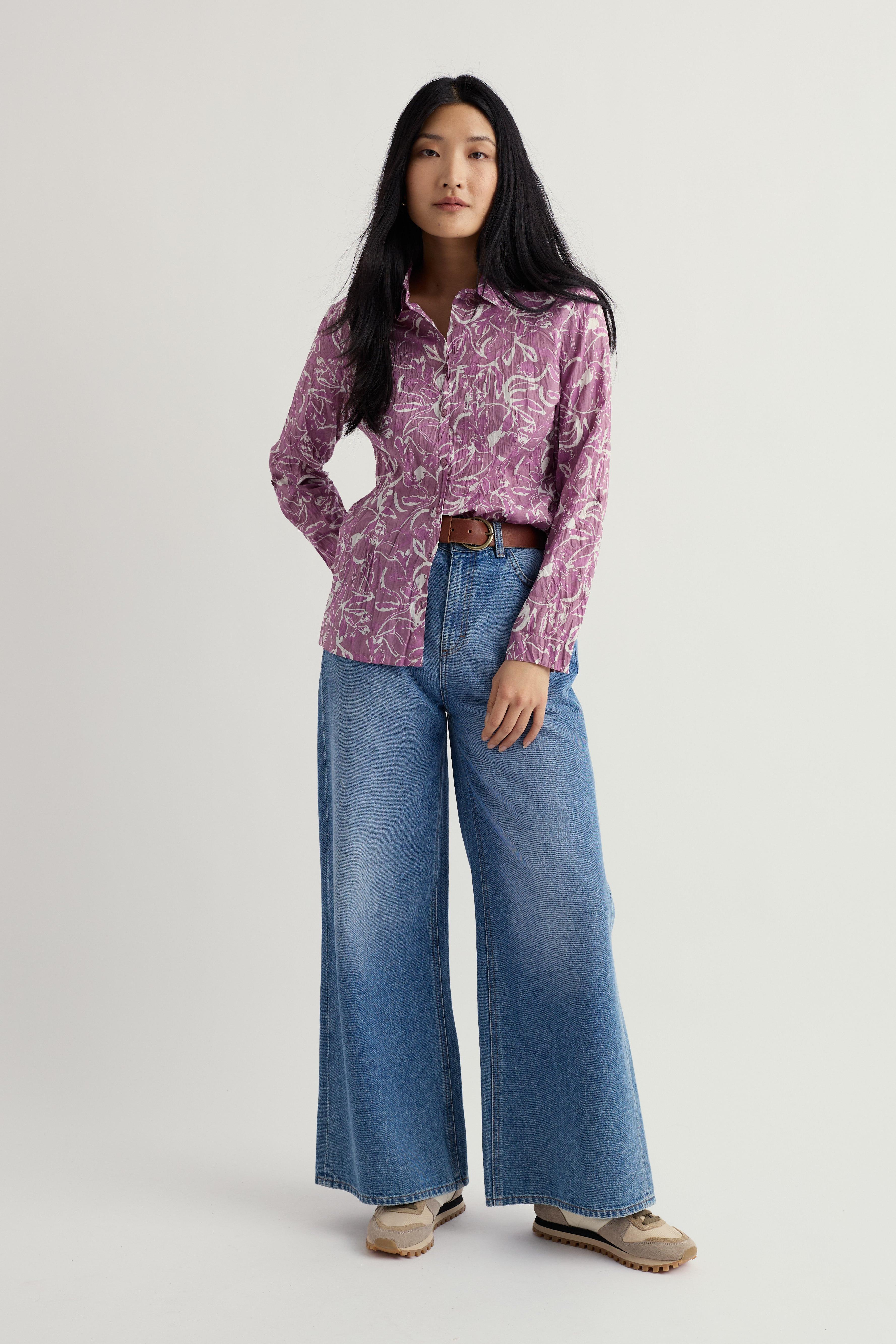 Woman wearing a purple organic cotton shirt and blue jeans on a white background
