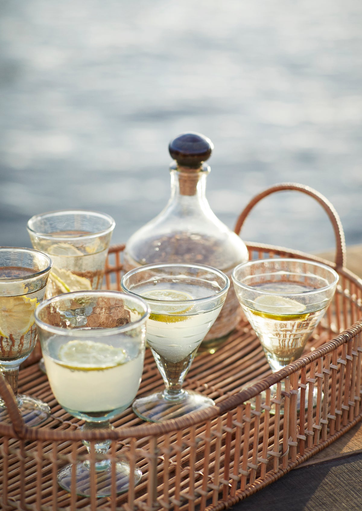 Madam Stoltz textured glass drinkware and a glass decanter on a decorative rattan tray with lemon slices.