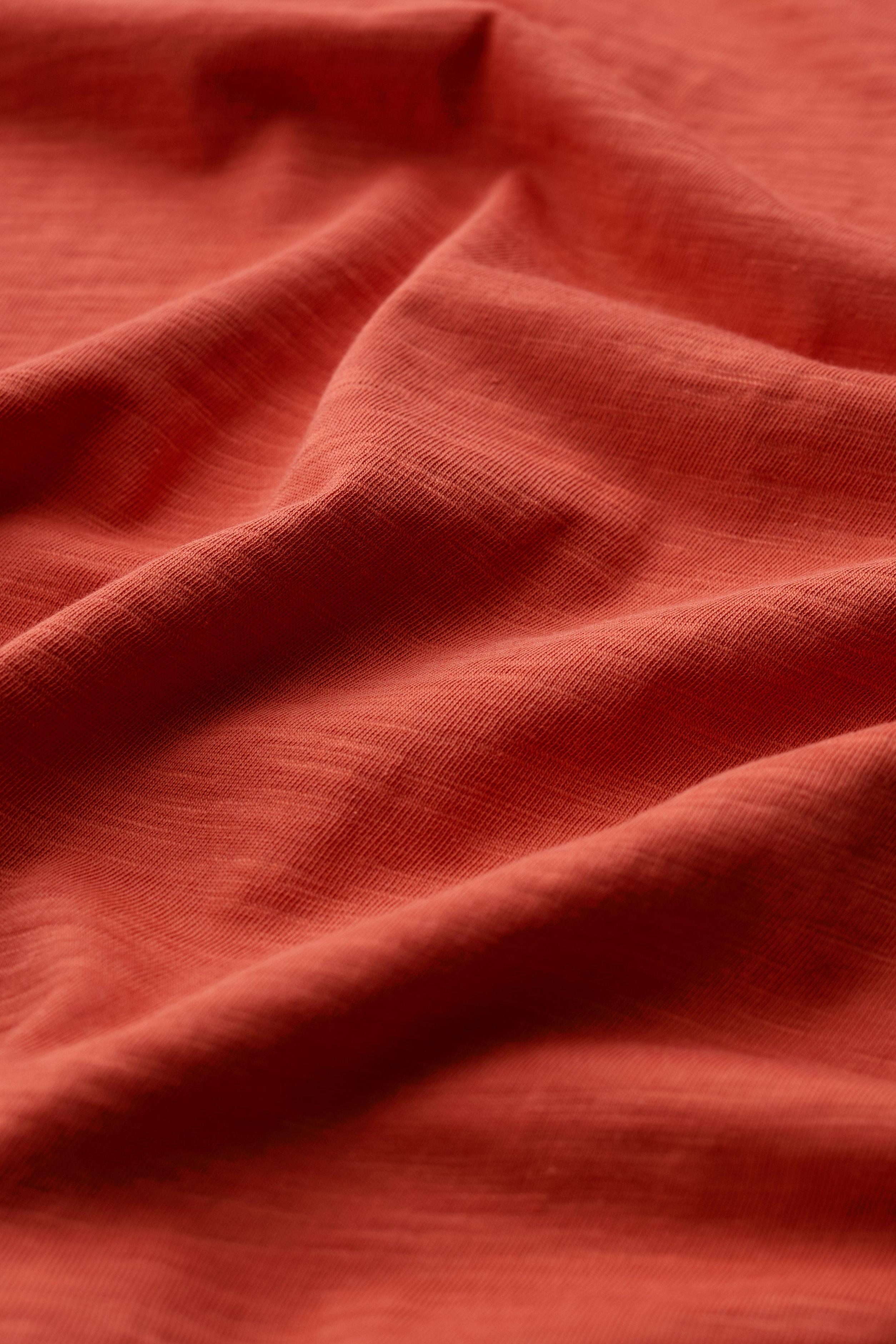 Close-up of red organic cotton fabric with soft, draped folds and visible textile texture.