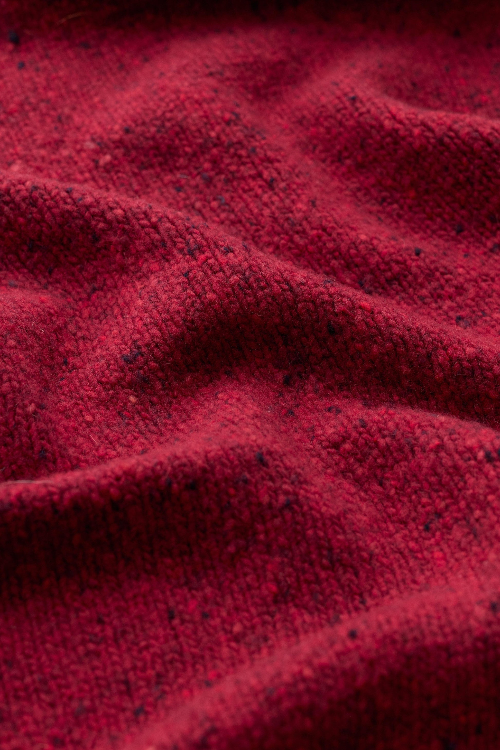 A close-up view of a soft red wool knit scarf featuring a textured, woven pattern.