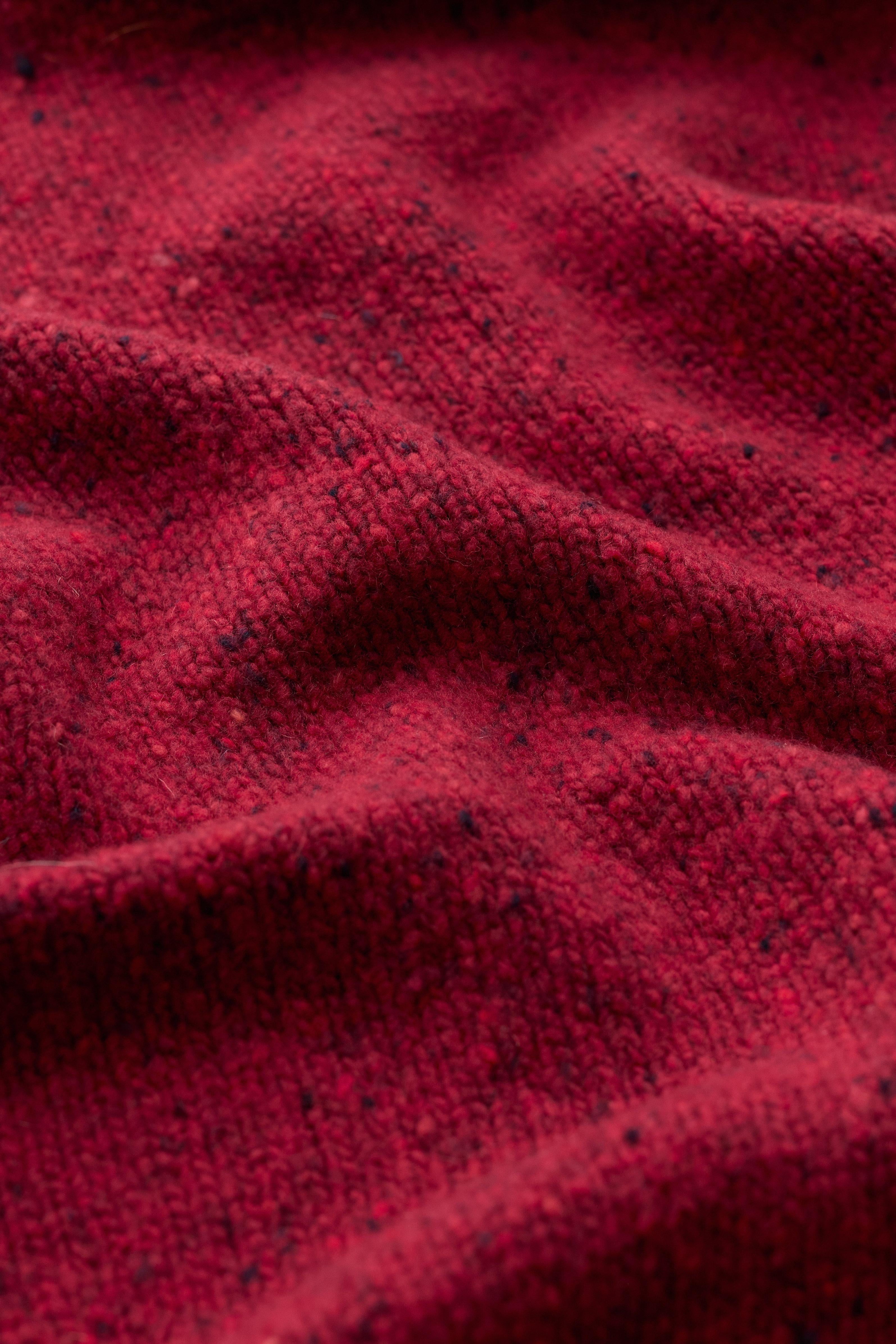 A close-up view of a soft red wool knit scarf featuring a textured, woven pattern.