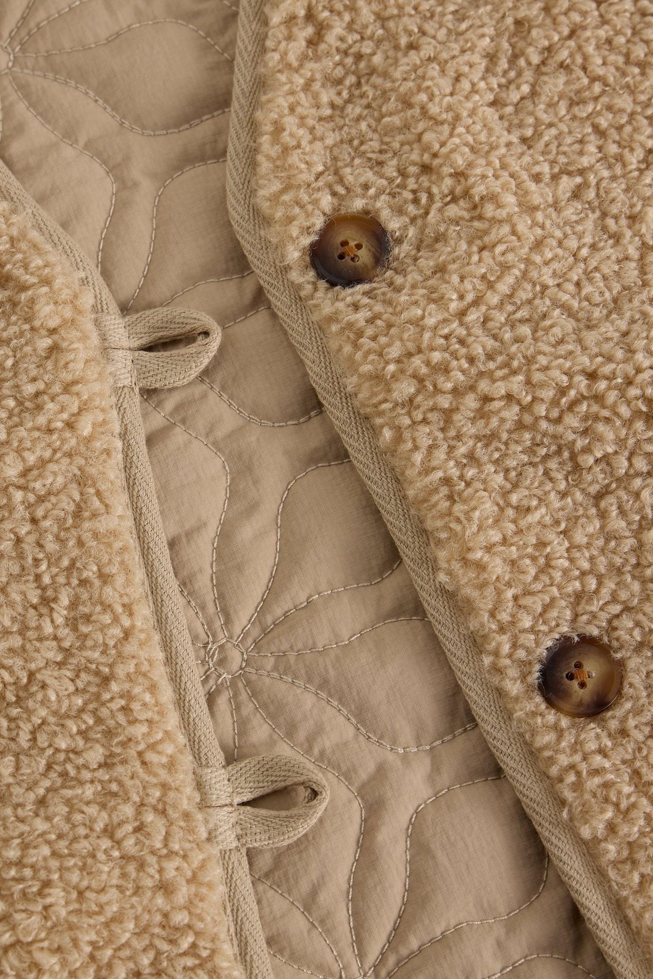 Close up of a cosy reversible women's gilet featuring textured fleece and quilted neutral fabric with button detail.