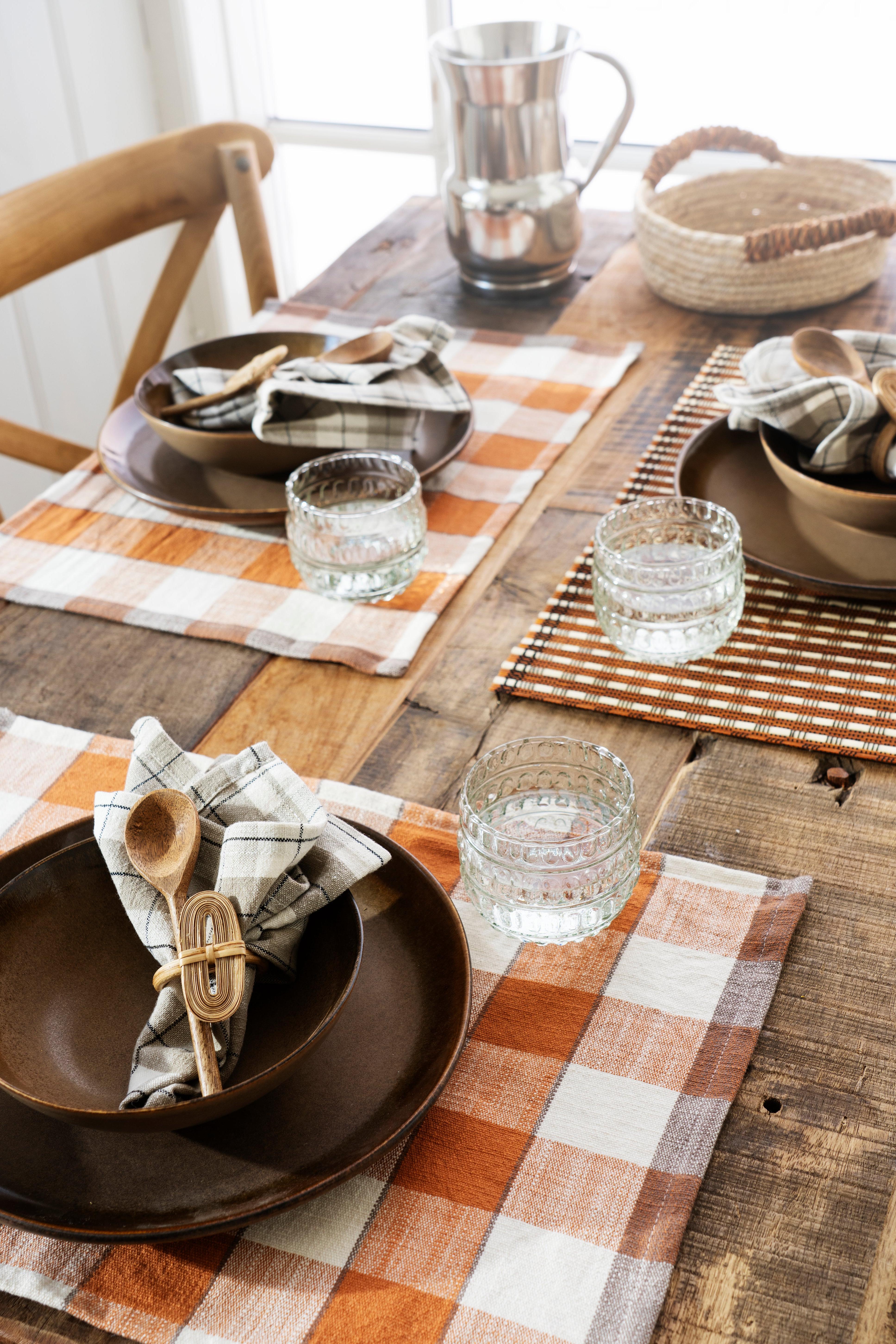 Dining table setting with checkered placemats, brown plates, and glasses.