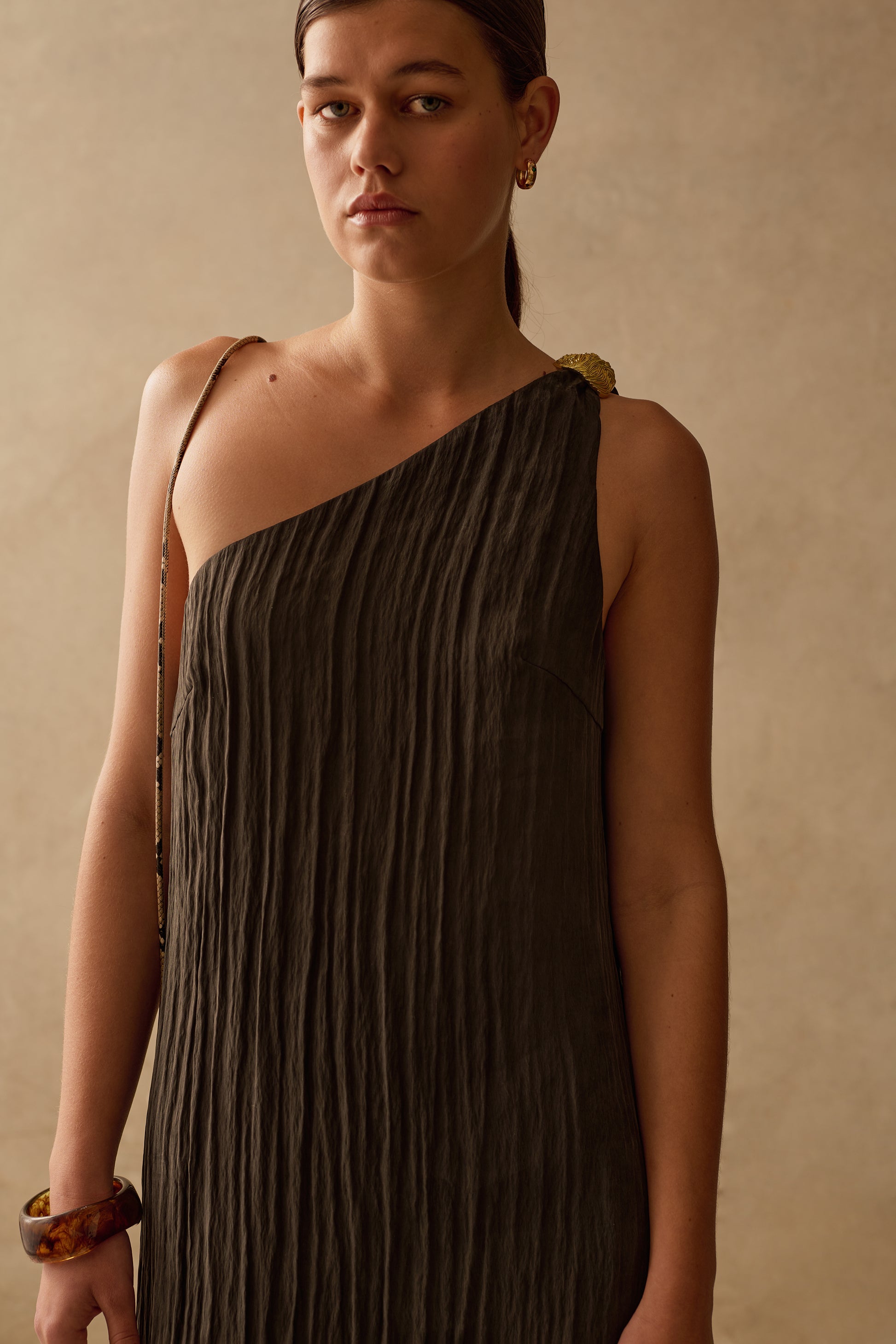Woman wearing a Sancia assymetrical one-shoulder dress against a beige background