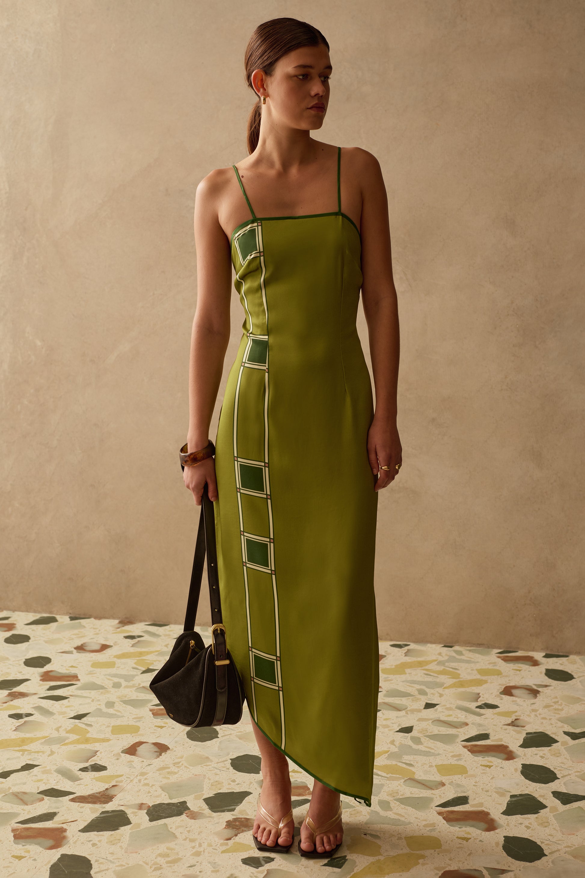Woman wearing a green dress with geometric patterns on a terrazzo floor and beige wall background