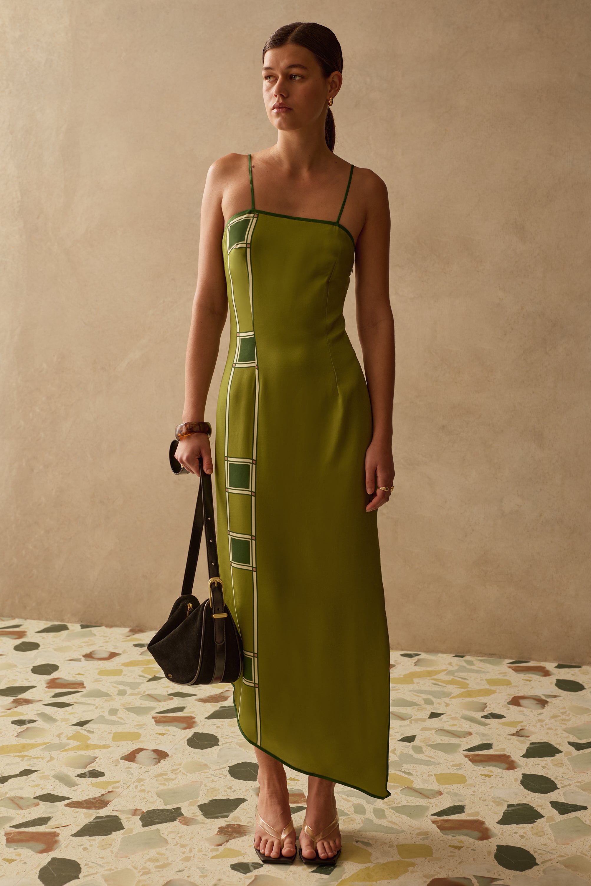 Woman wearing a green dress with square patterns, standing against a beige wall.