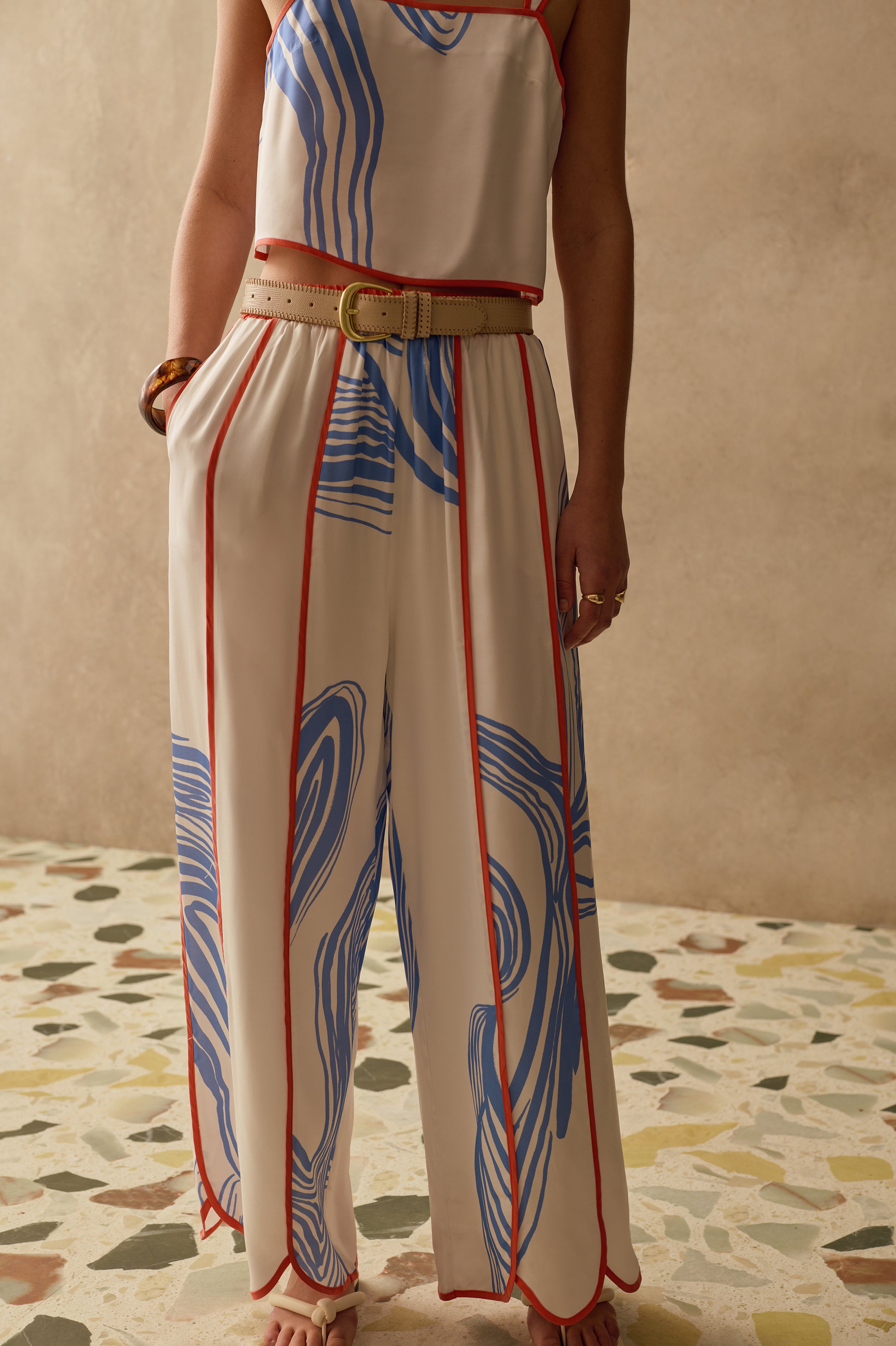 Person wearing patterned wide leg trousers with a belt on a textured floor.