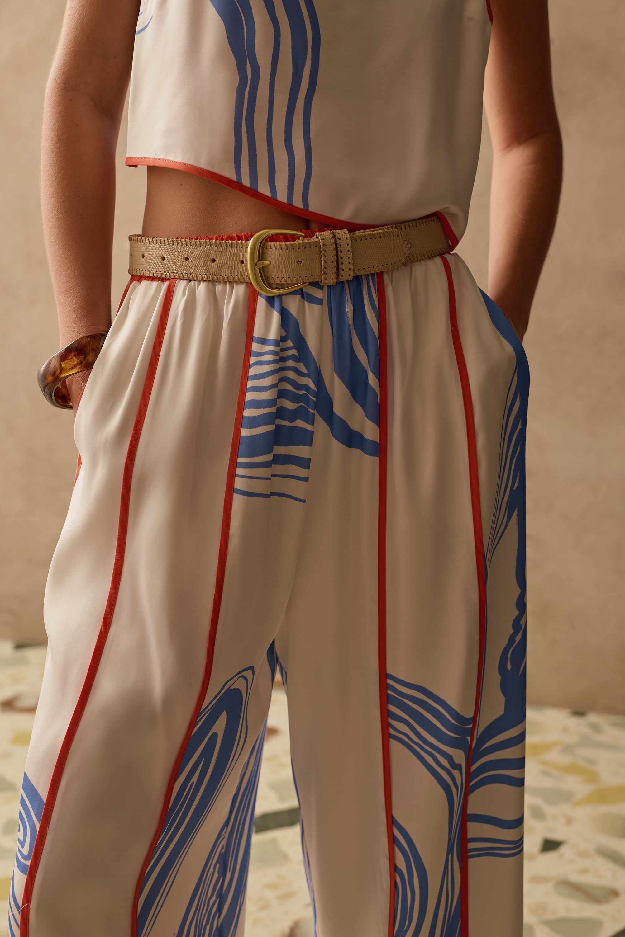 Person wearing a sleeveless top and wide leg pants with abstract patterns on a sandy background