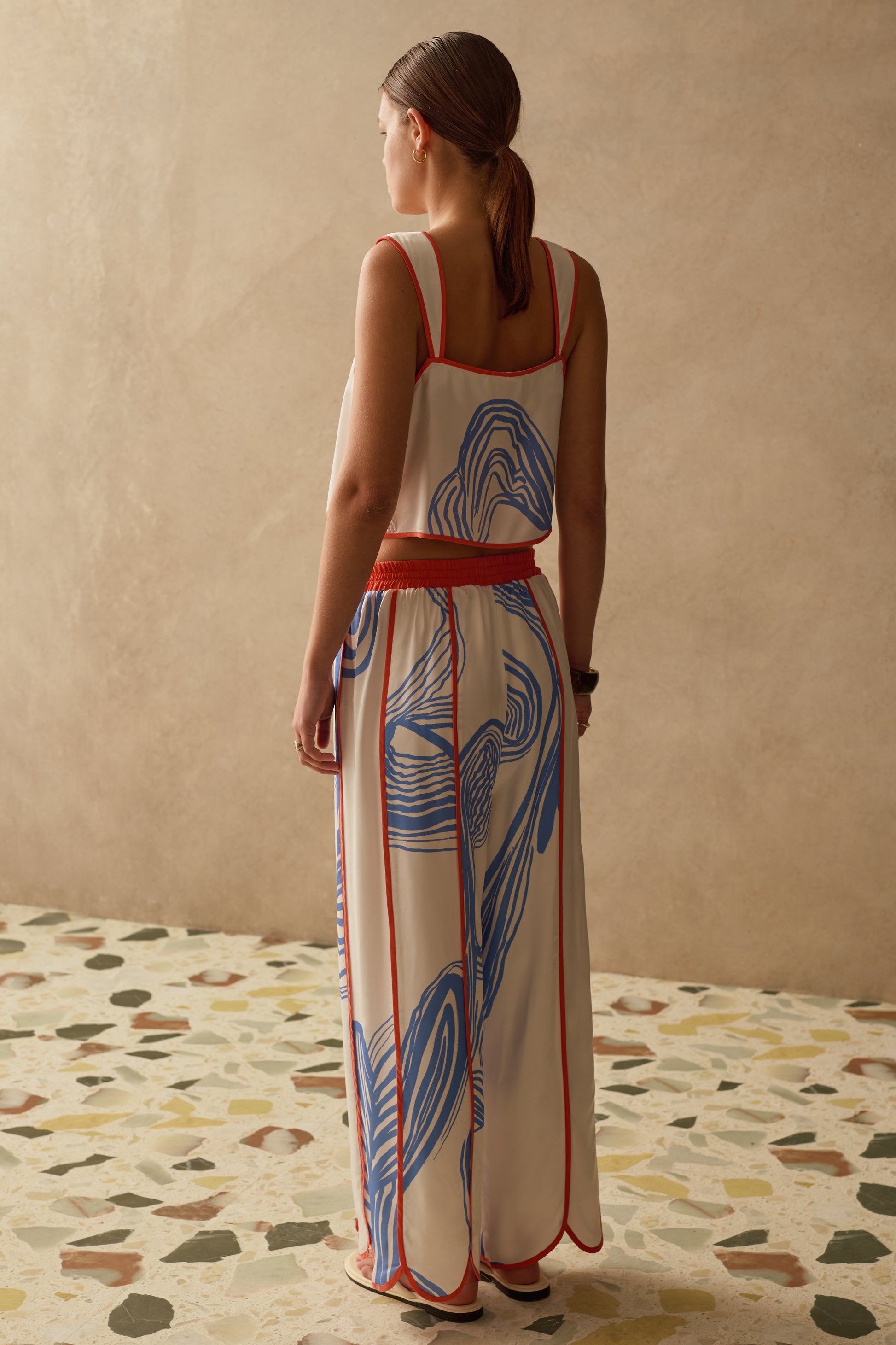 Woman wearing a patterned outfit standing in a room with a textured wall and patterned floor.
