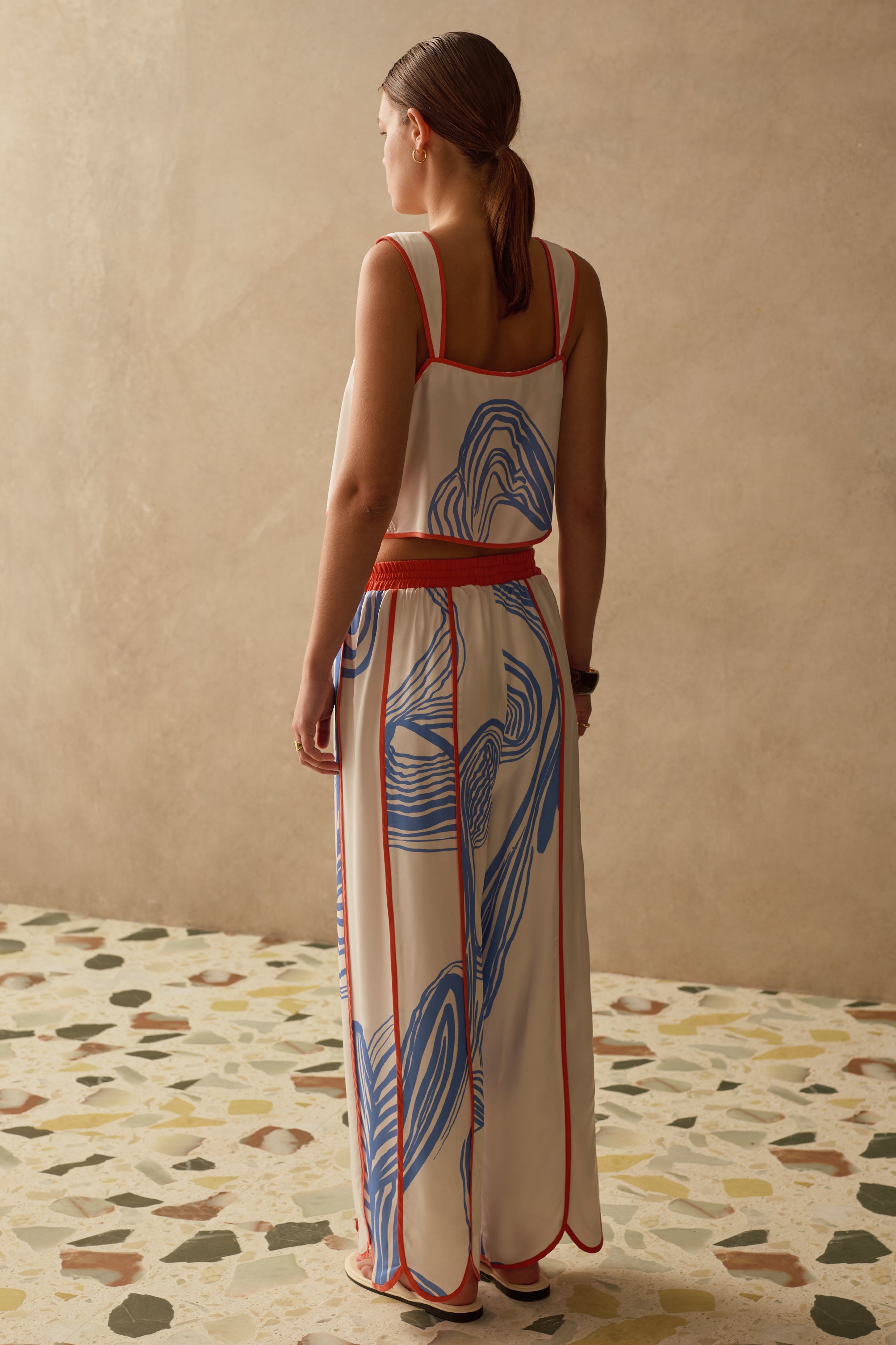 Woman wearing a patterned outfit standing in a room with a textured wall and patterned floor.