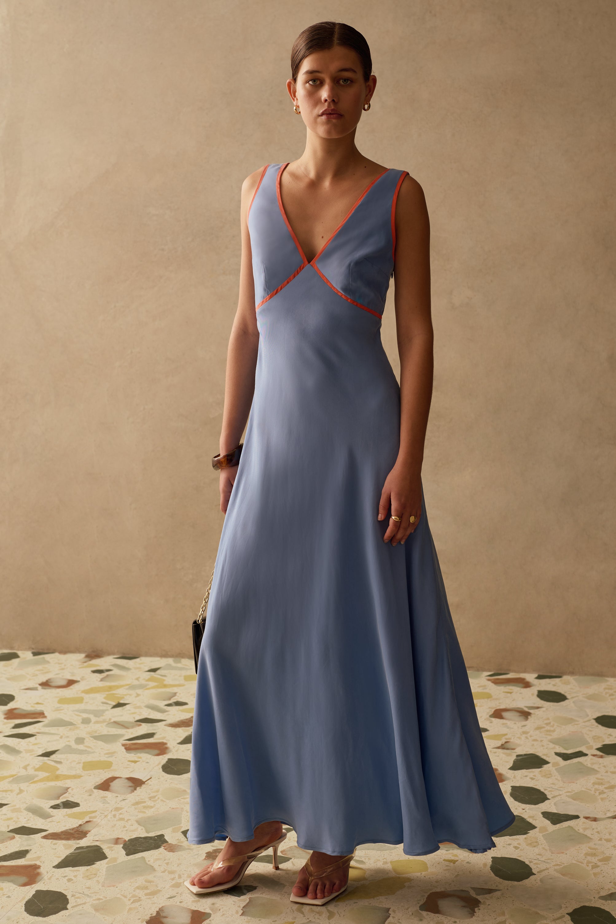 Woman wearing a blue v neck dress with orange accents against a beige wall.