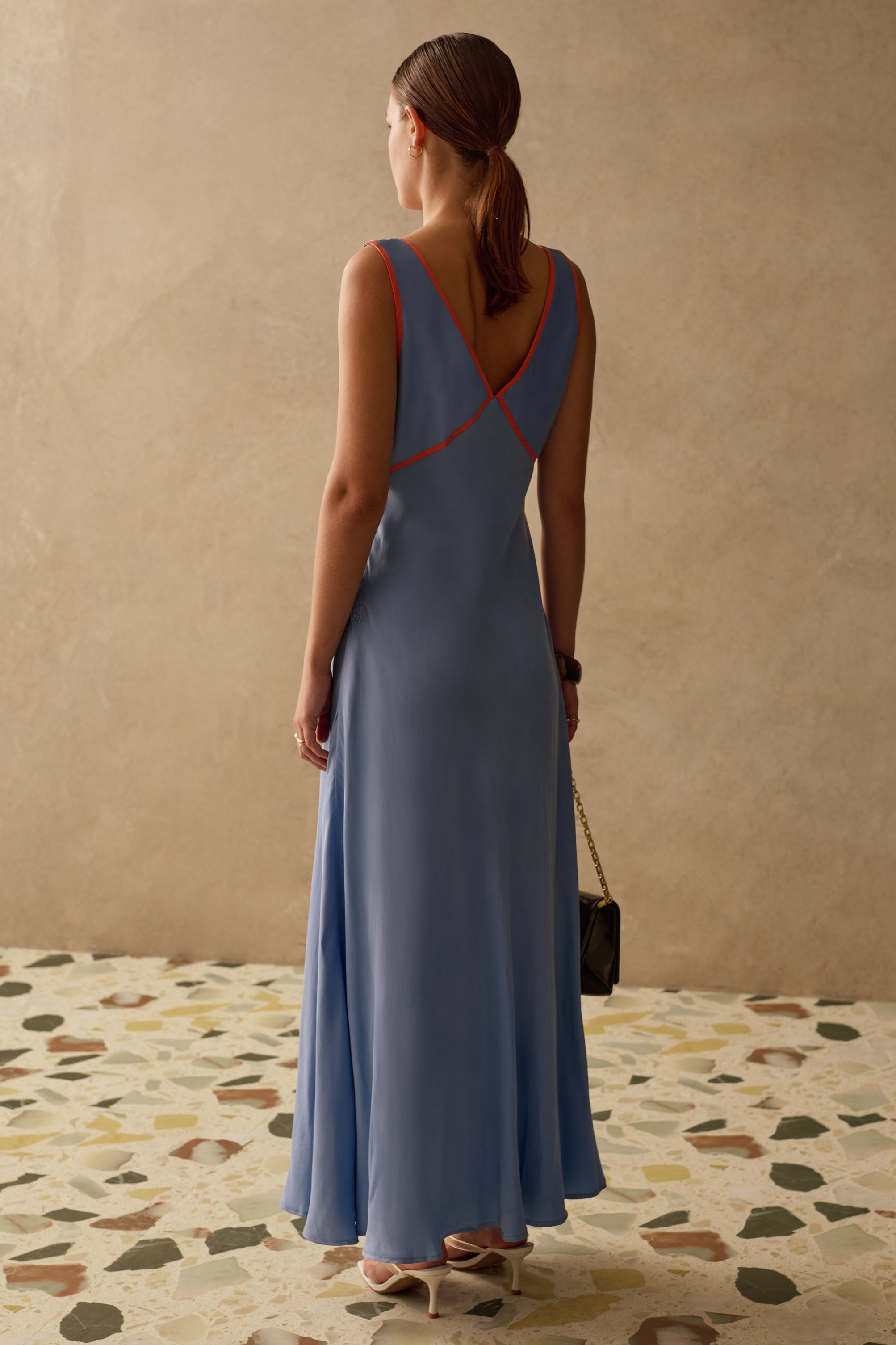 Woman in a blue wedding guest dress standing in a room with a textured floor and beige wall.