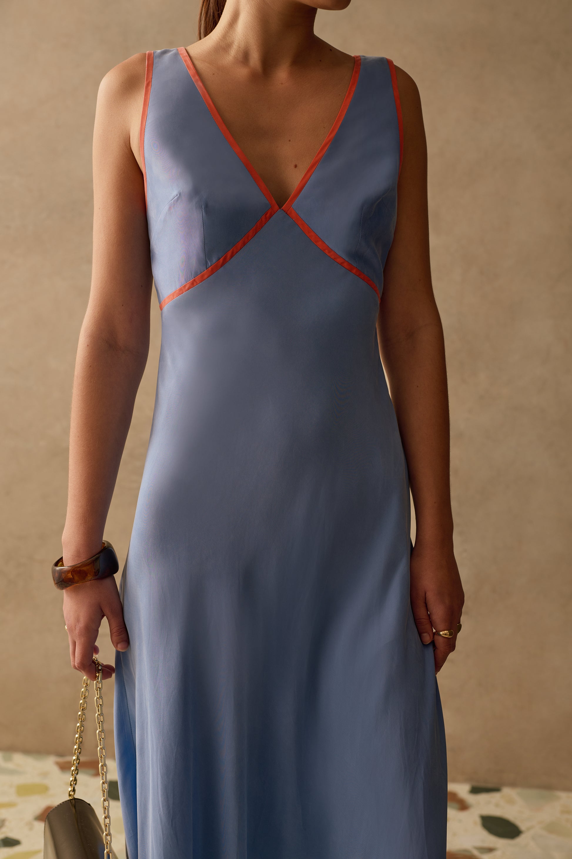 Woman wearing a blue dress with red accents against a beige wall.
