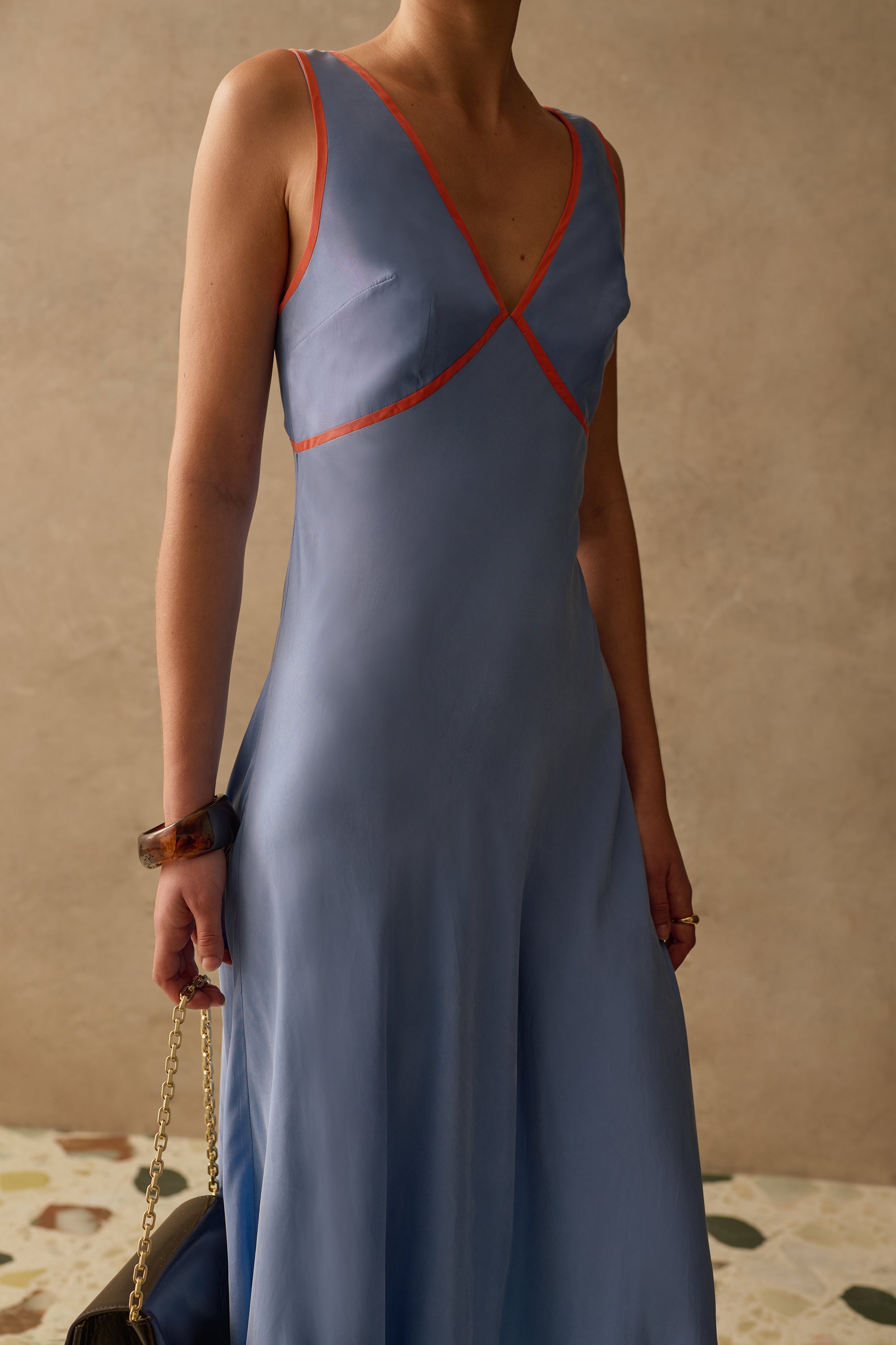 Woman wearing a blue v-neck sleeveless dress with red accents against a beige wall.