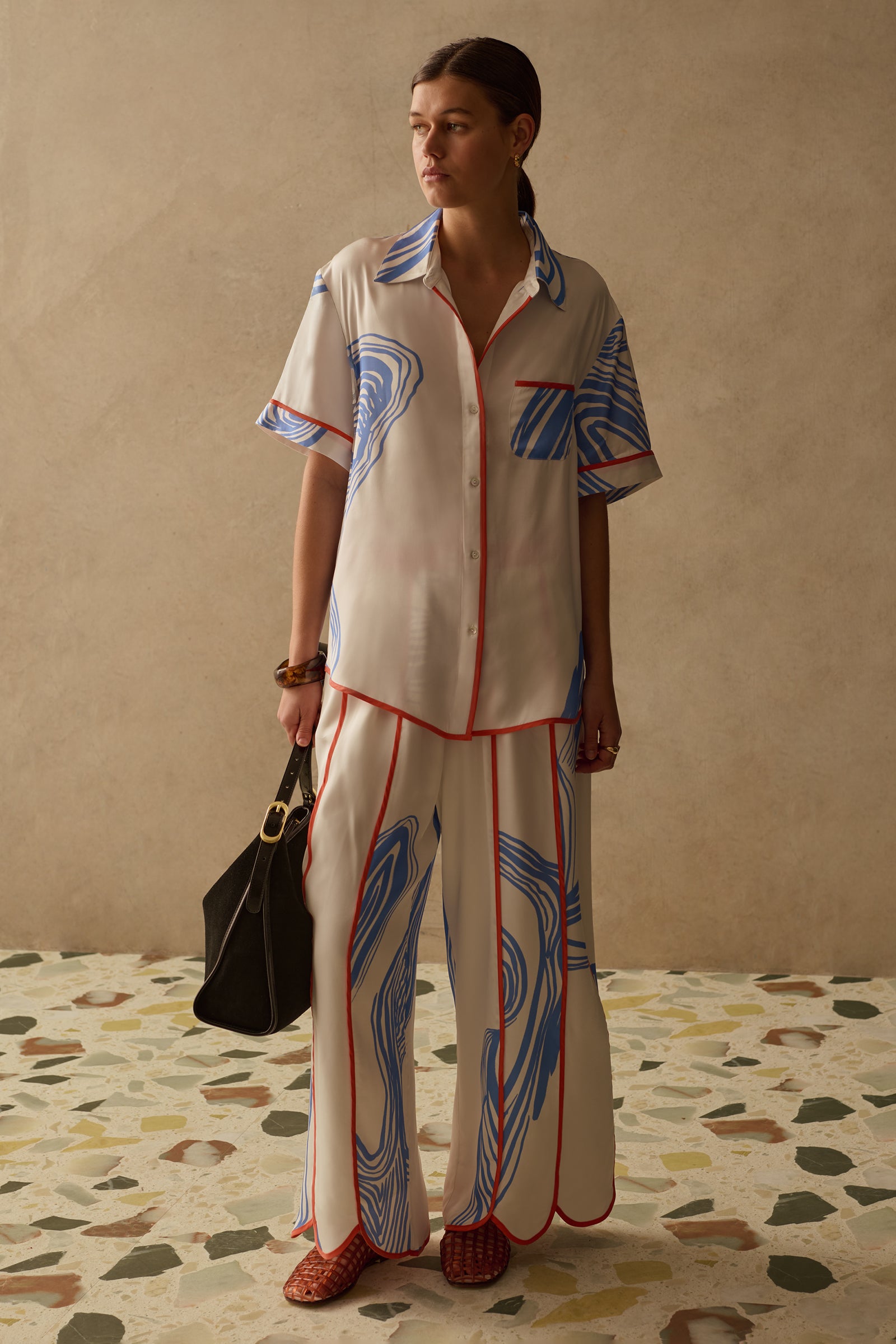Woman wearing a patterned summer outfit standing on a terrazzo floor with a beige wall background