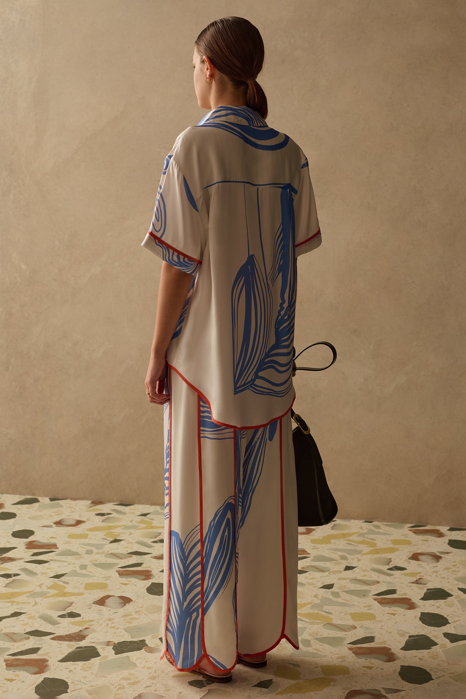 Woman wearing a patterned Sancia co-ord standing on a terrazzo floor with a beige wall background