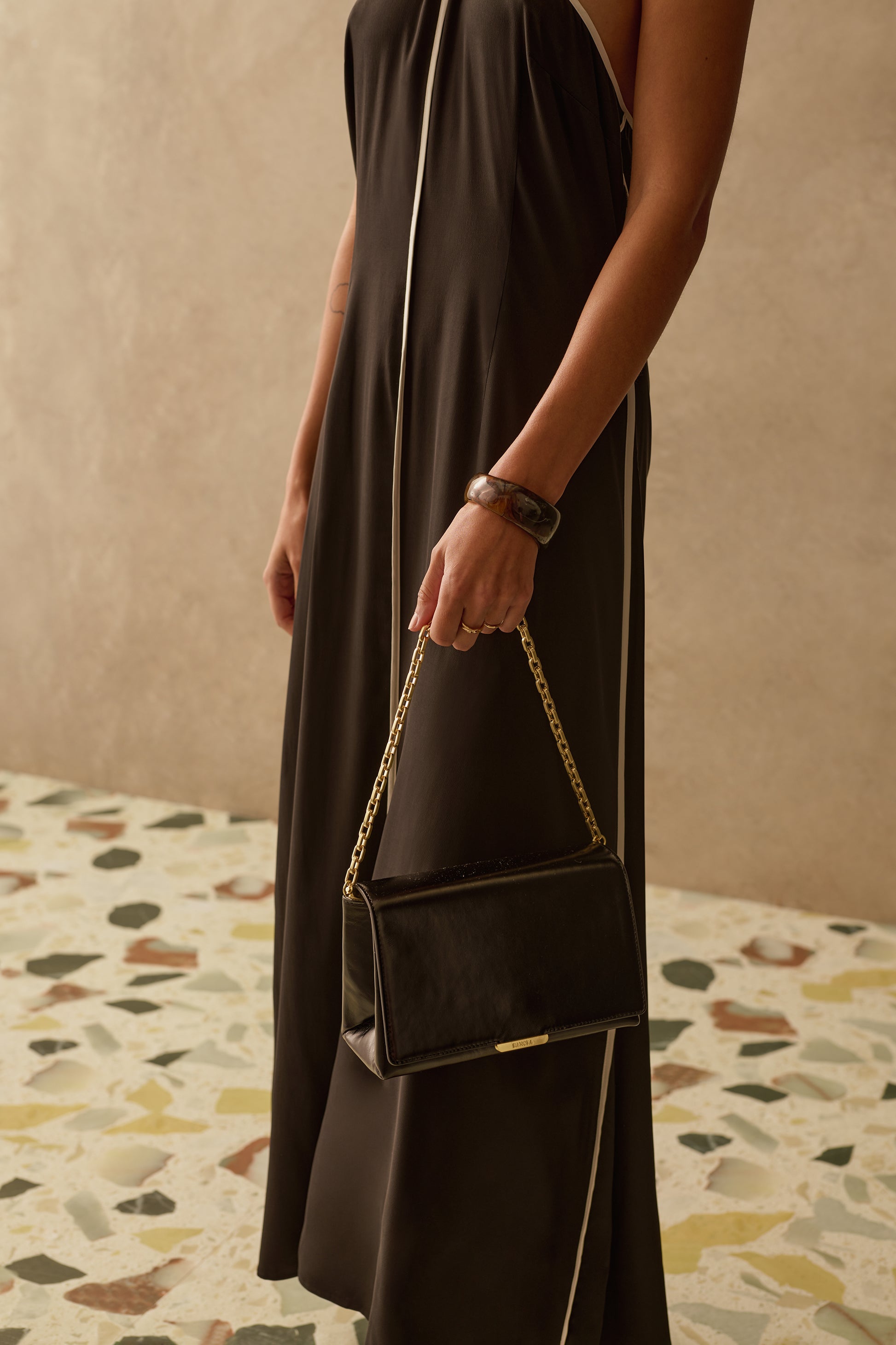 Model wearing a black and white halter neck dress with black bag with gold chain
