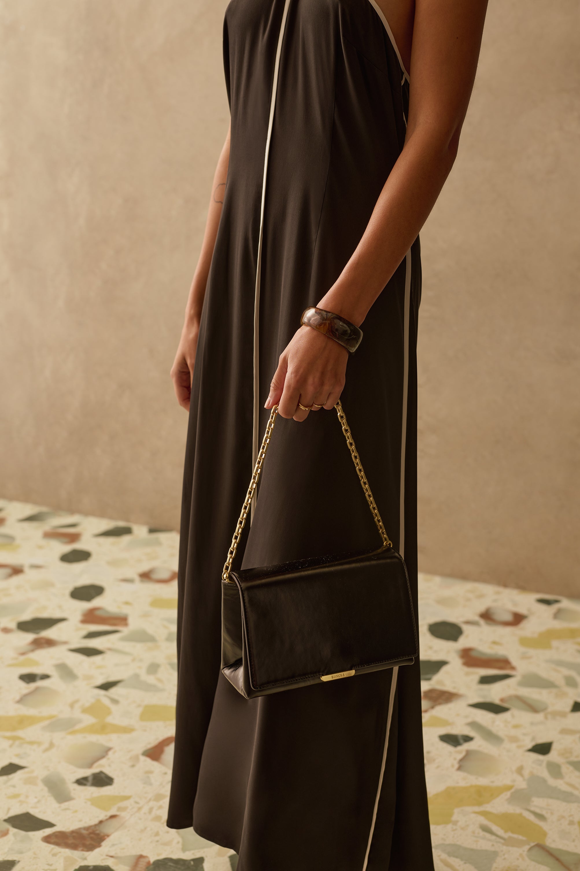 Model wearing a black and white halter neck dress with black bag with gold chain