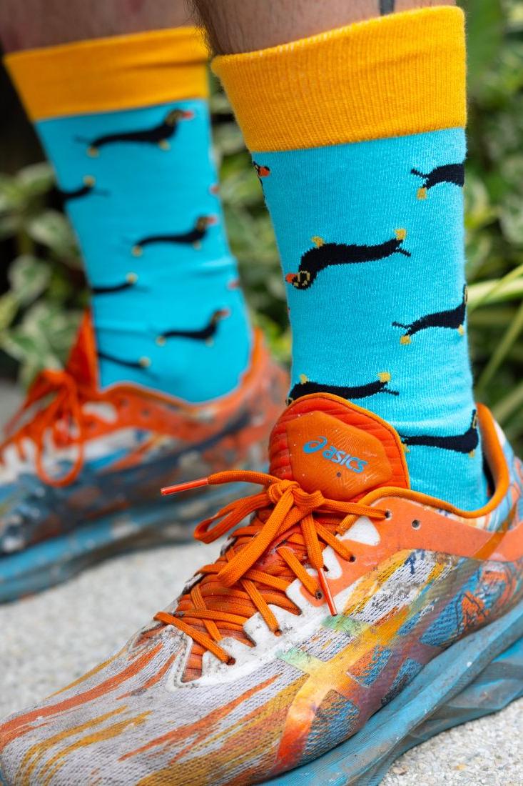 Close-up of bright blue bamboo socks with sausage dog pattern worn with orange and blue patterned running shoes.