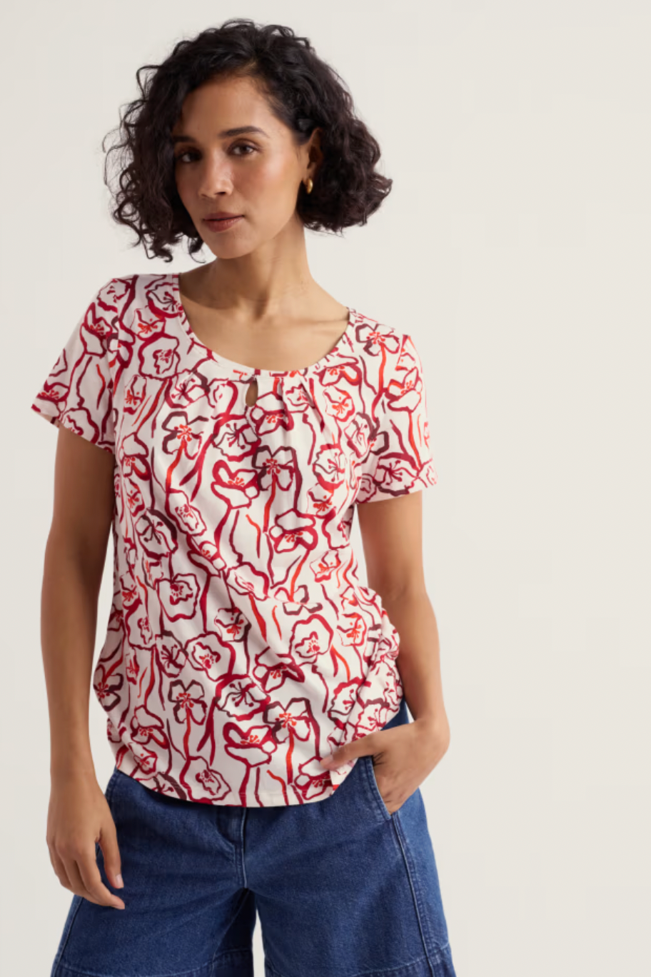 Woman wearing a red and white patterned top with blue jeans on a plain background