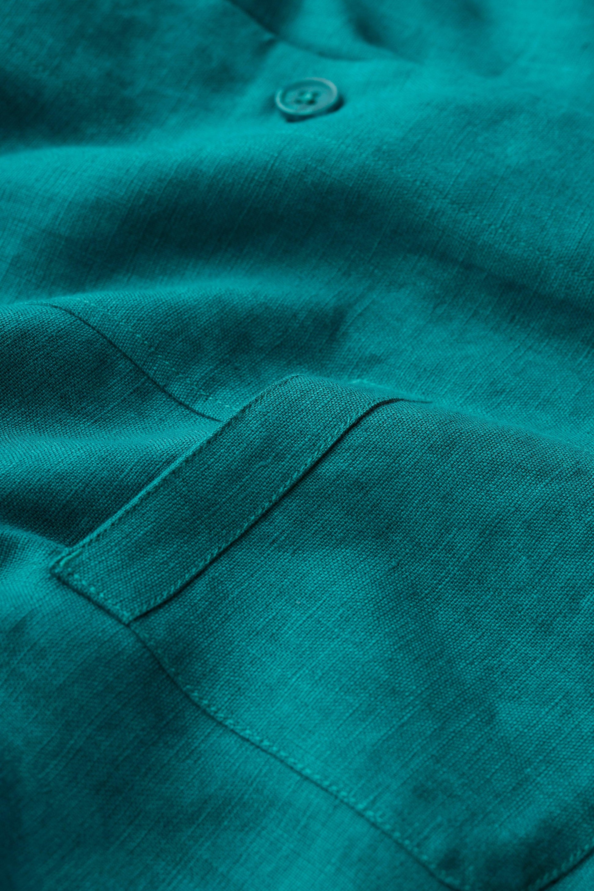 Close-up of a teal linen jacket with a button and pocket detail.