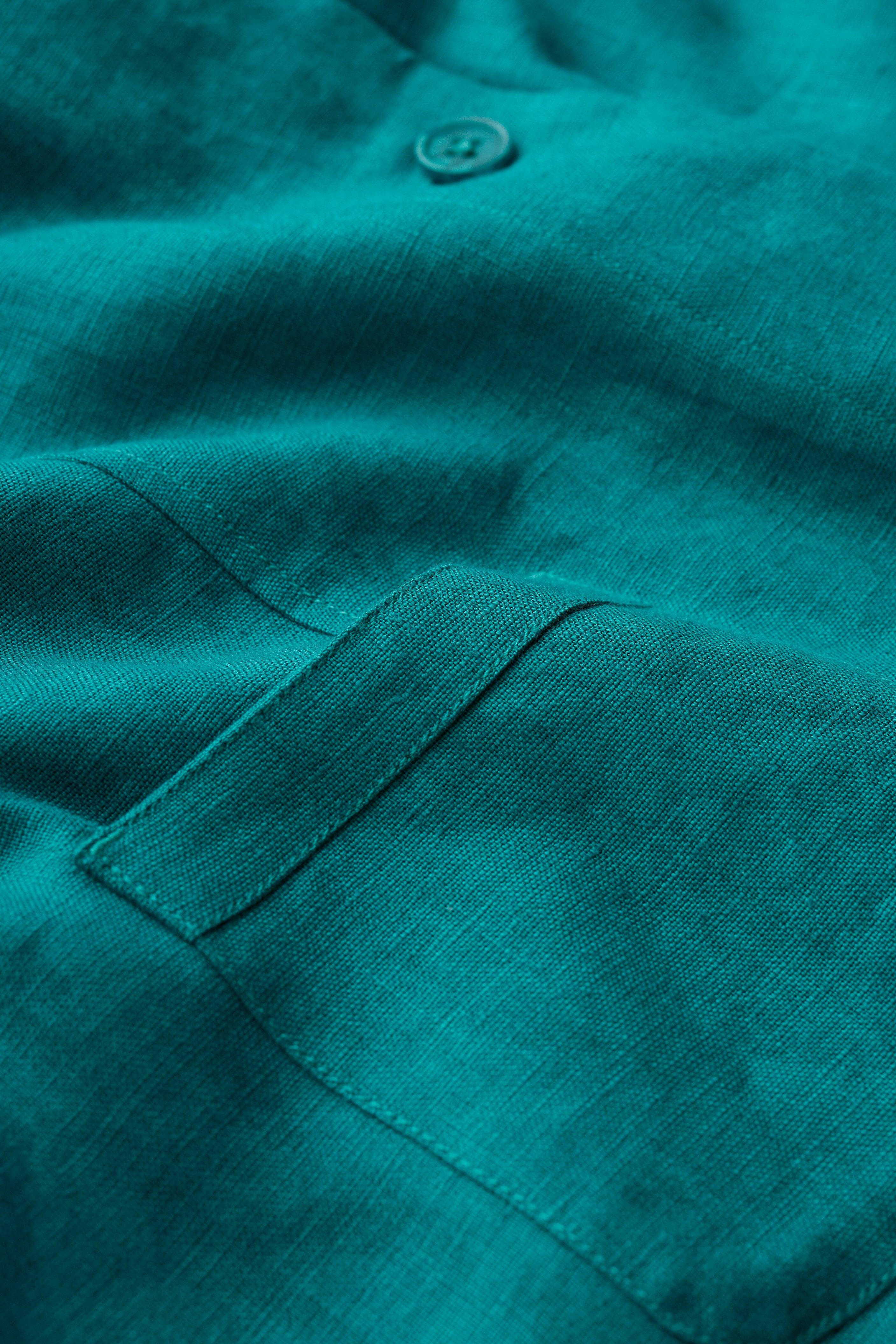 Close-up of a teal linen jacket with a button and pocket detail.
