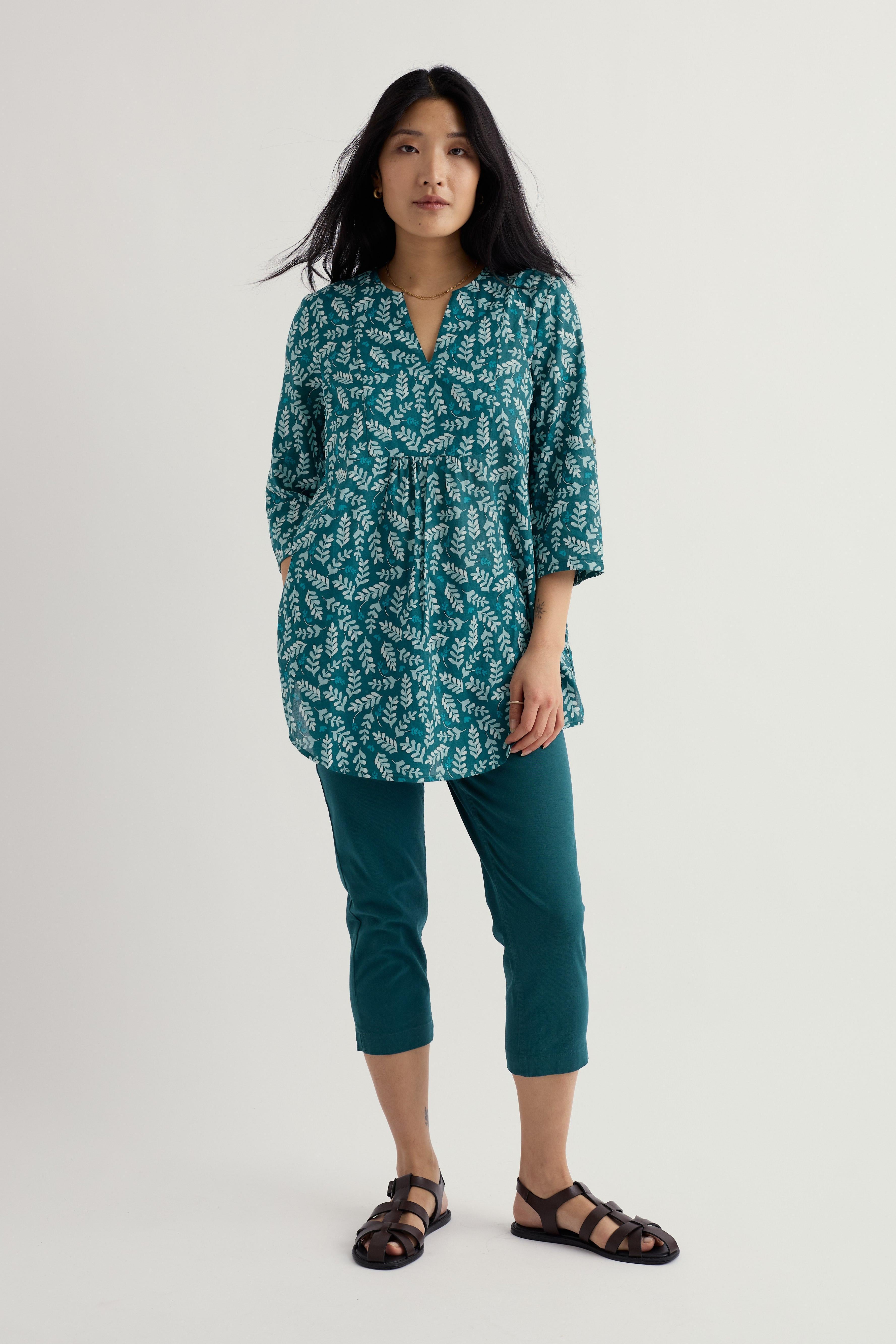 Woman wearing a teal patterned shirt and organic cotton pants on a white background