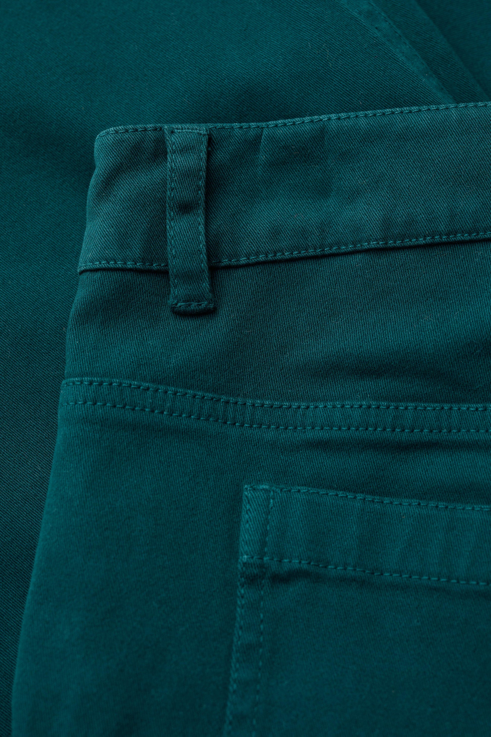 Close-up of teal organic cotton pants with a pocket and button detail.