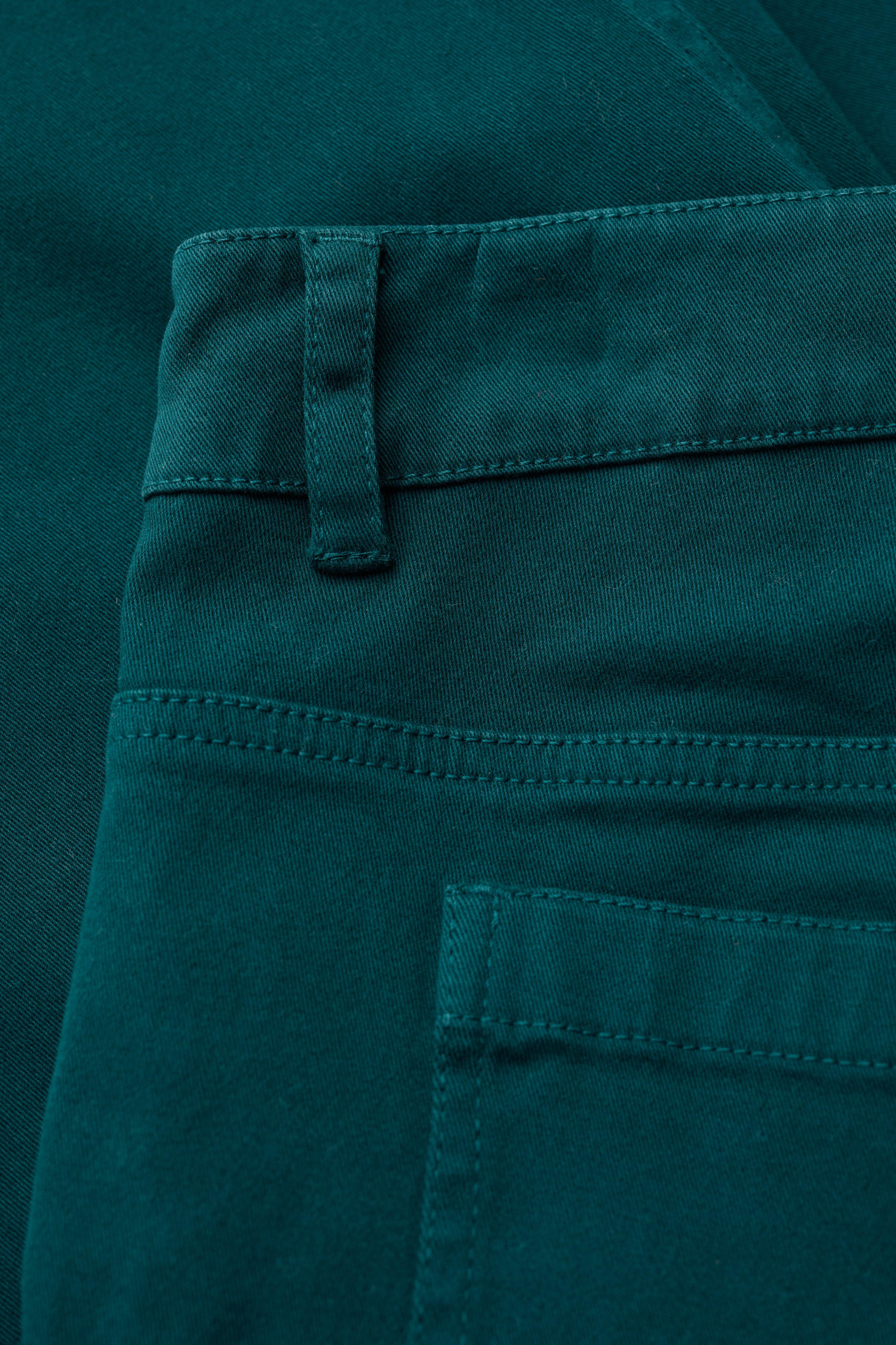 Close-up of teal organic cotton pants with a pocket and button detail.
