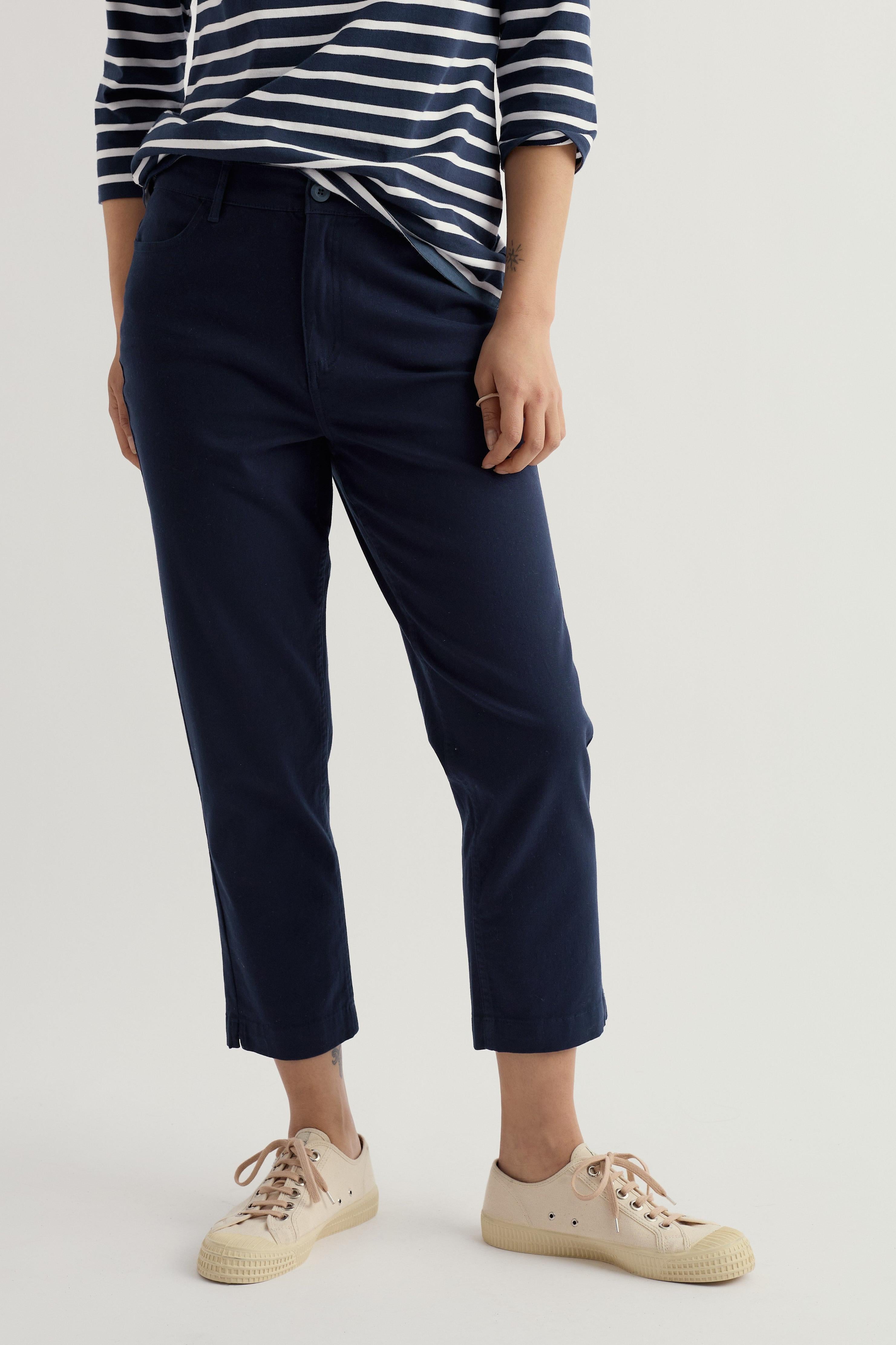 Person wearing navy cropped trousers and a striped shirt on a plain background