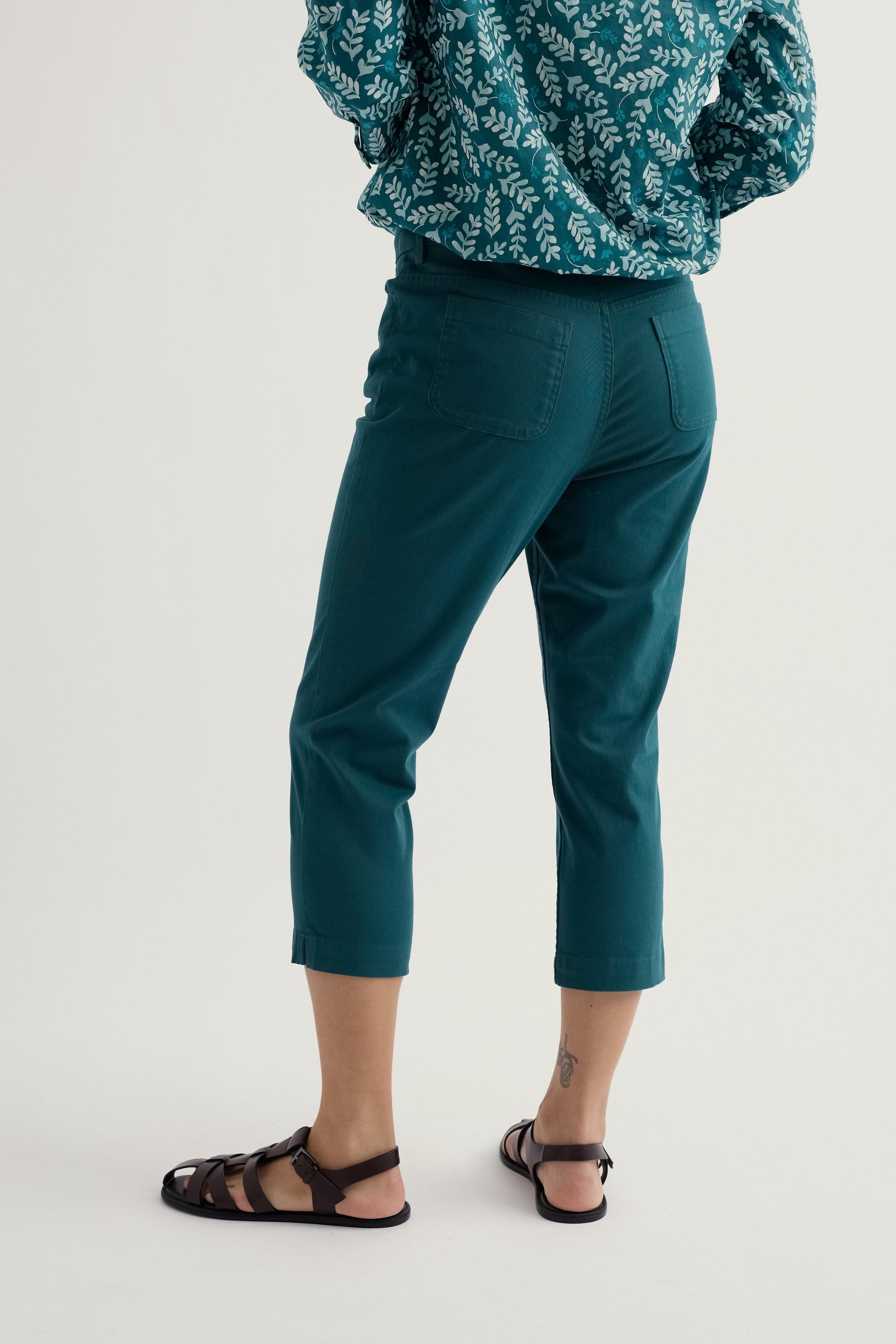Model wearing teal Seasalt slim leg pants and a patterned top on a light background