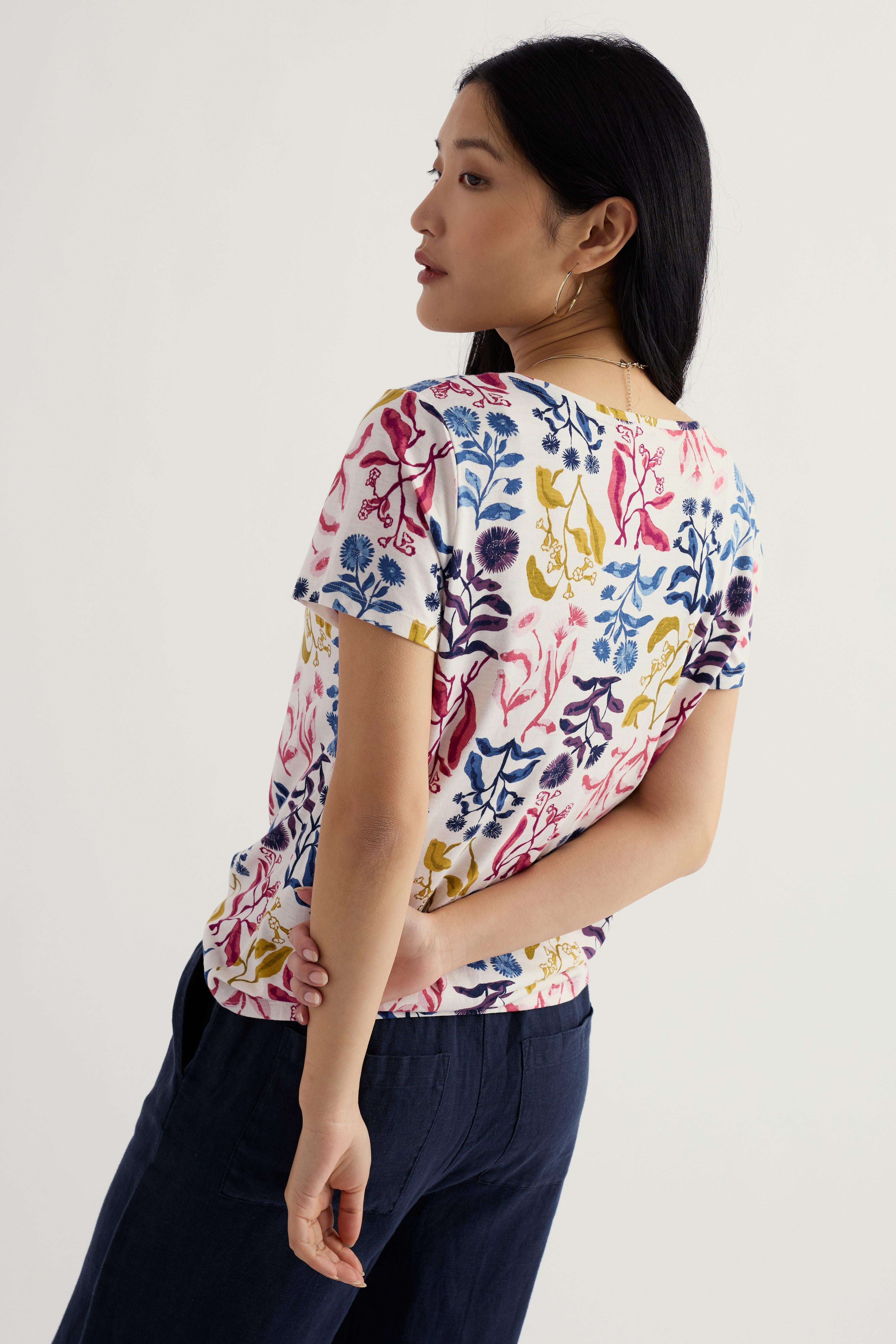 Woman wearing a colorful floral top and navy pants on a white background