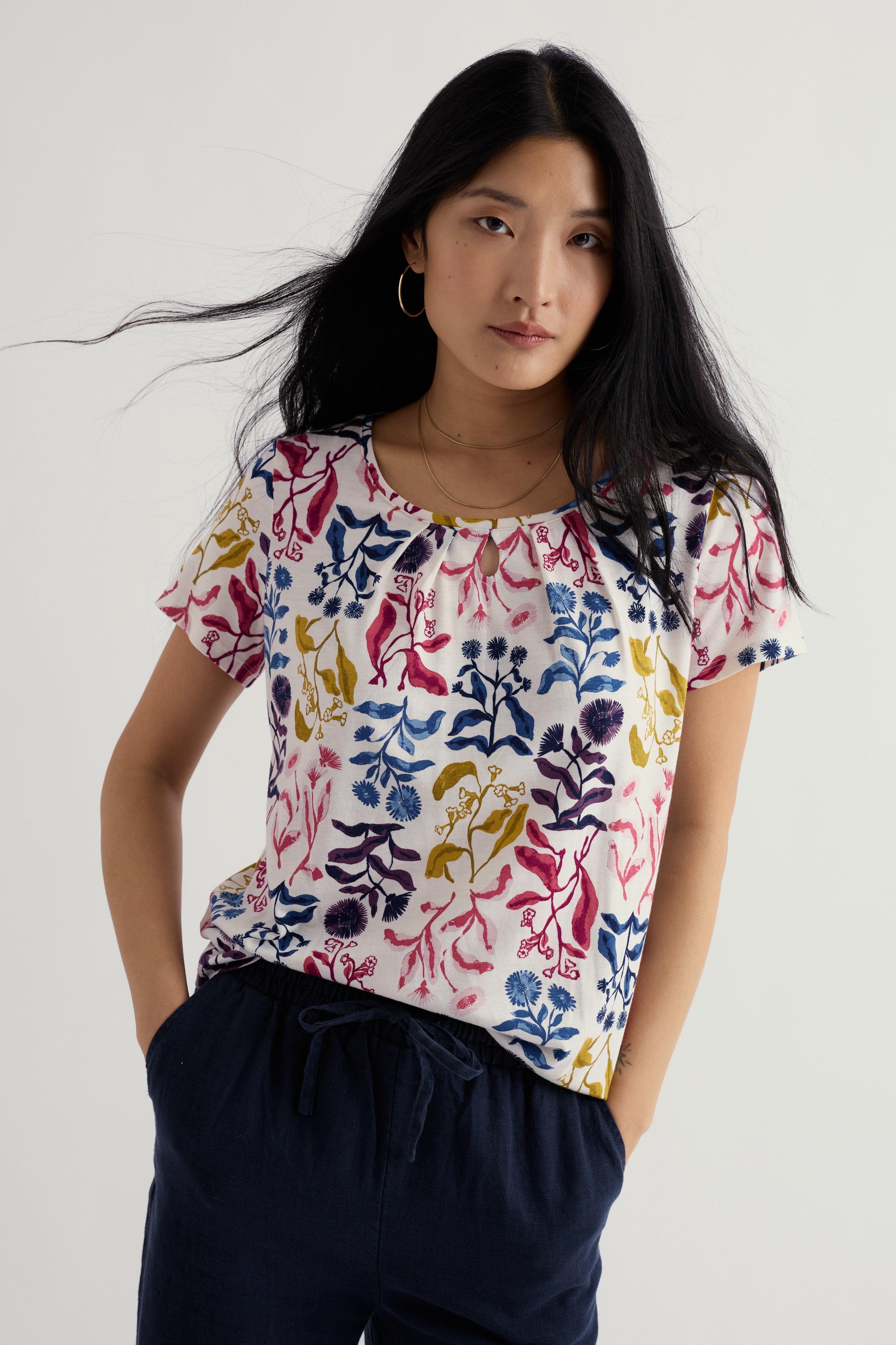 Woman wearing a colorful floral blouse with navy pants on a white background
