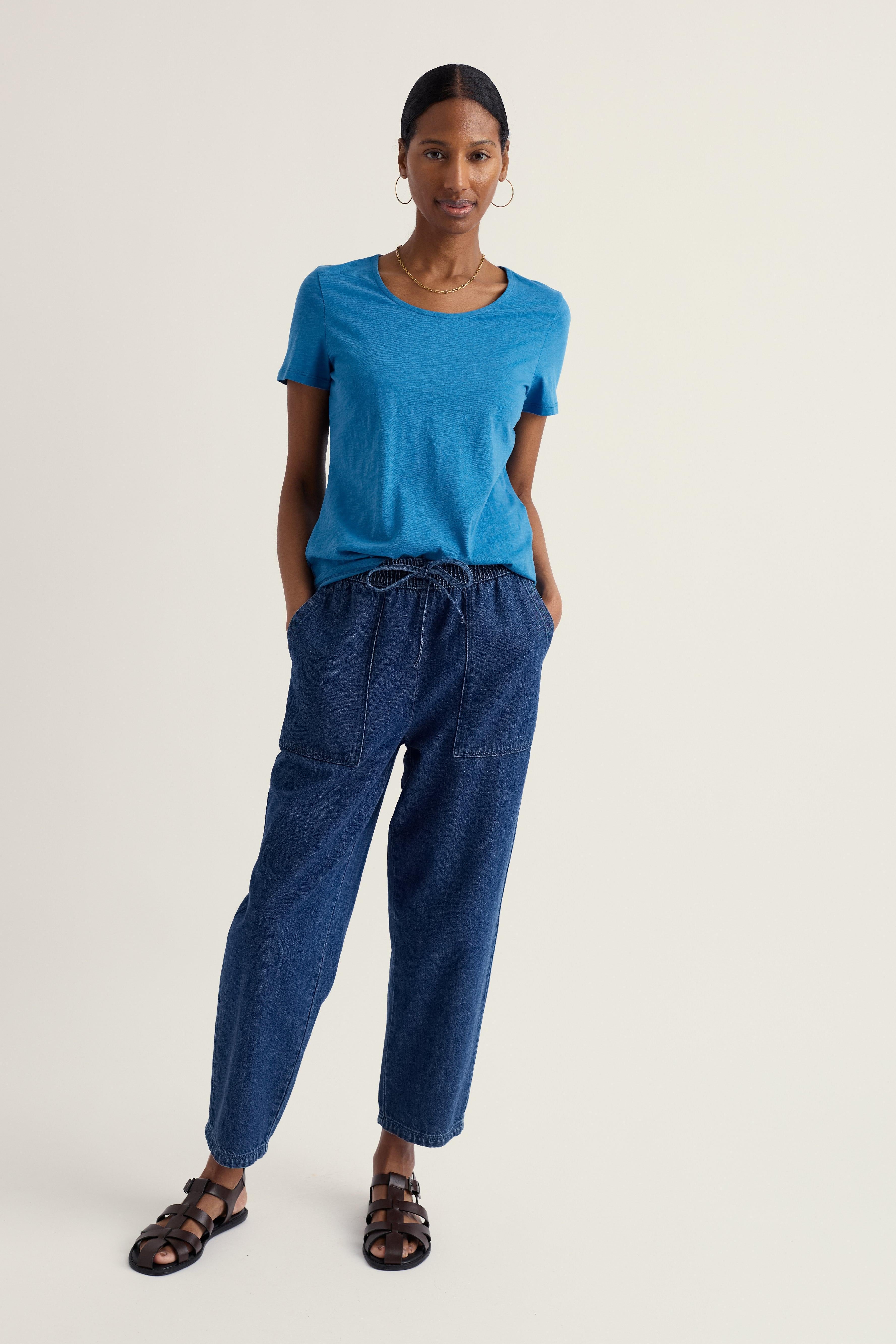 Woman wearing a blue Seasalt t-shirt and blue pants on a plain background